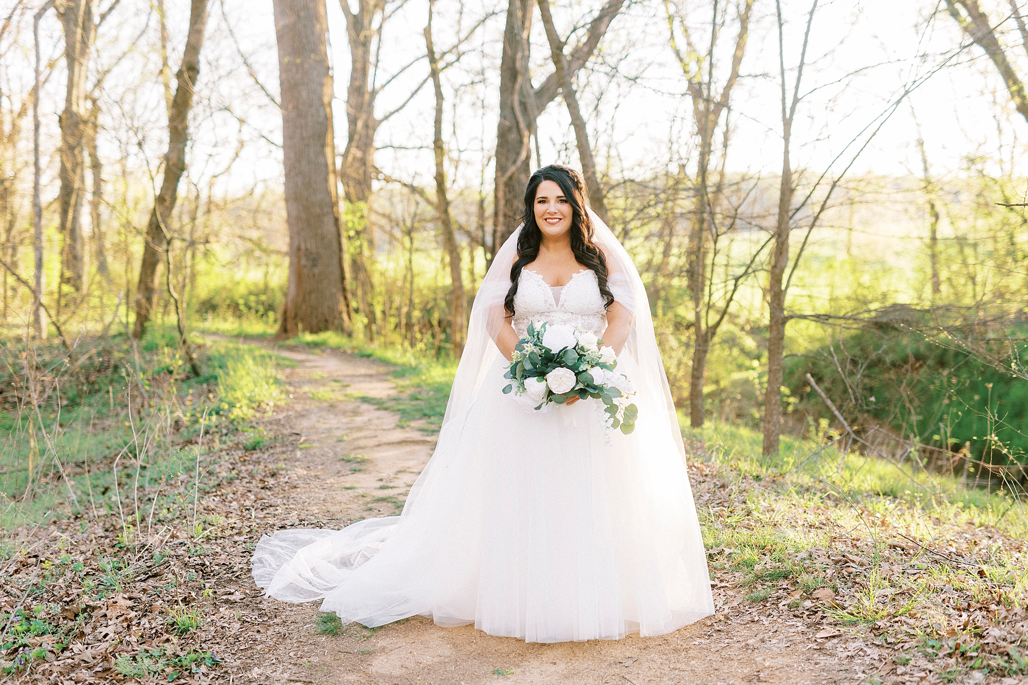 bride stands with veil around shoulders holding white bouquet in Sloan Park