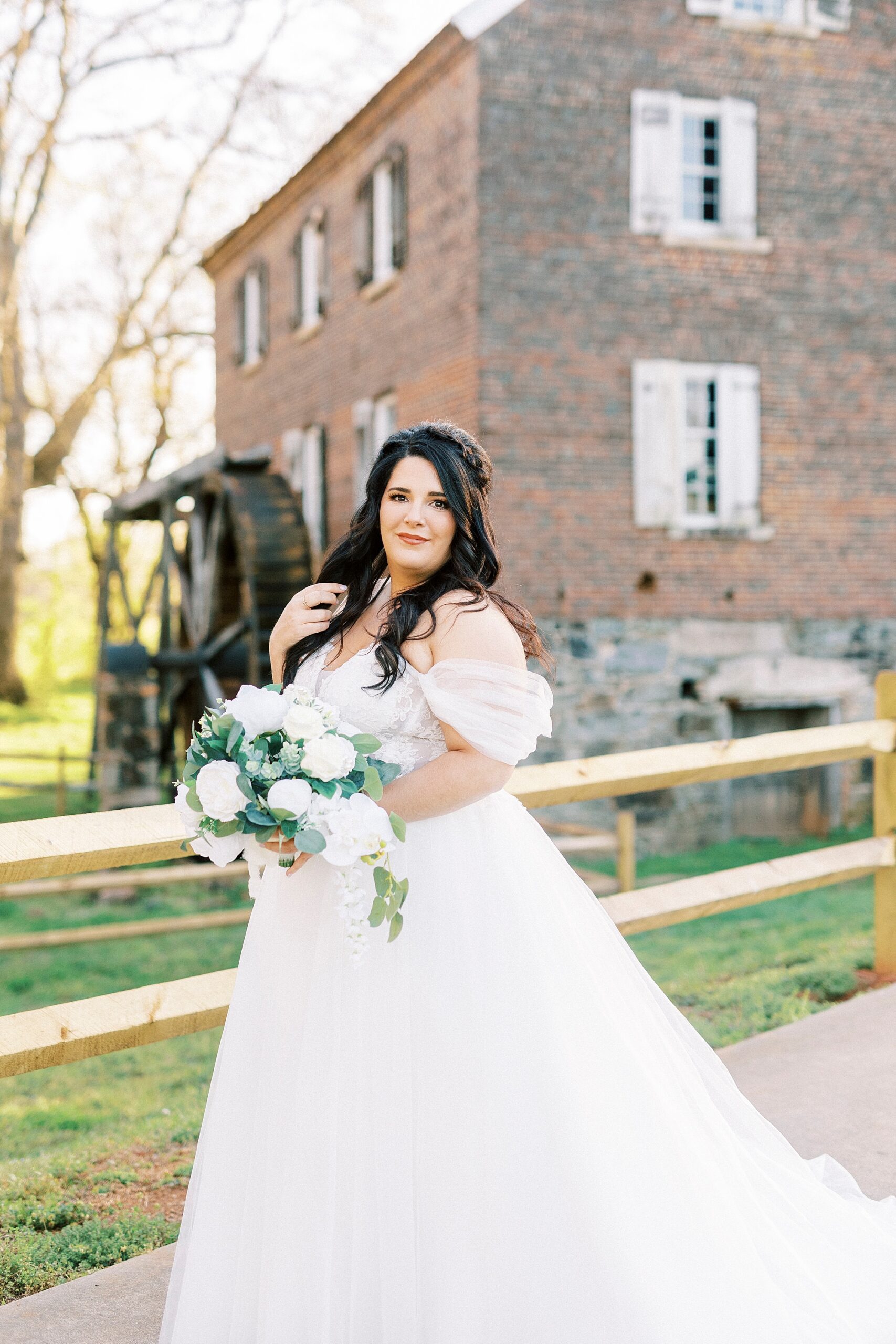 brunette bride holds bouquet of white flowers in front of brick building 