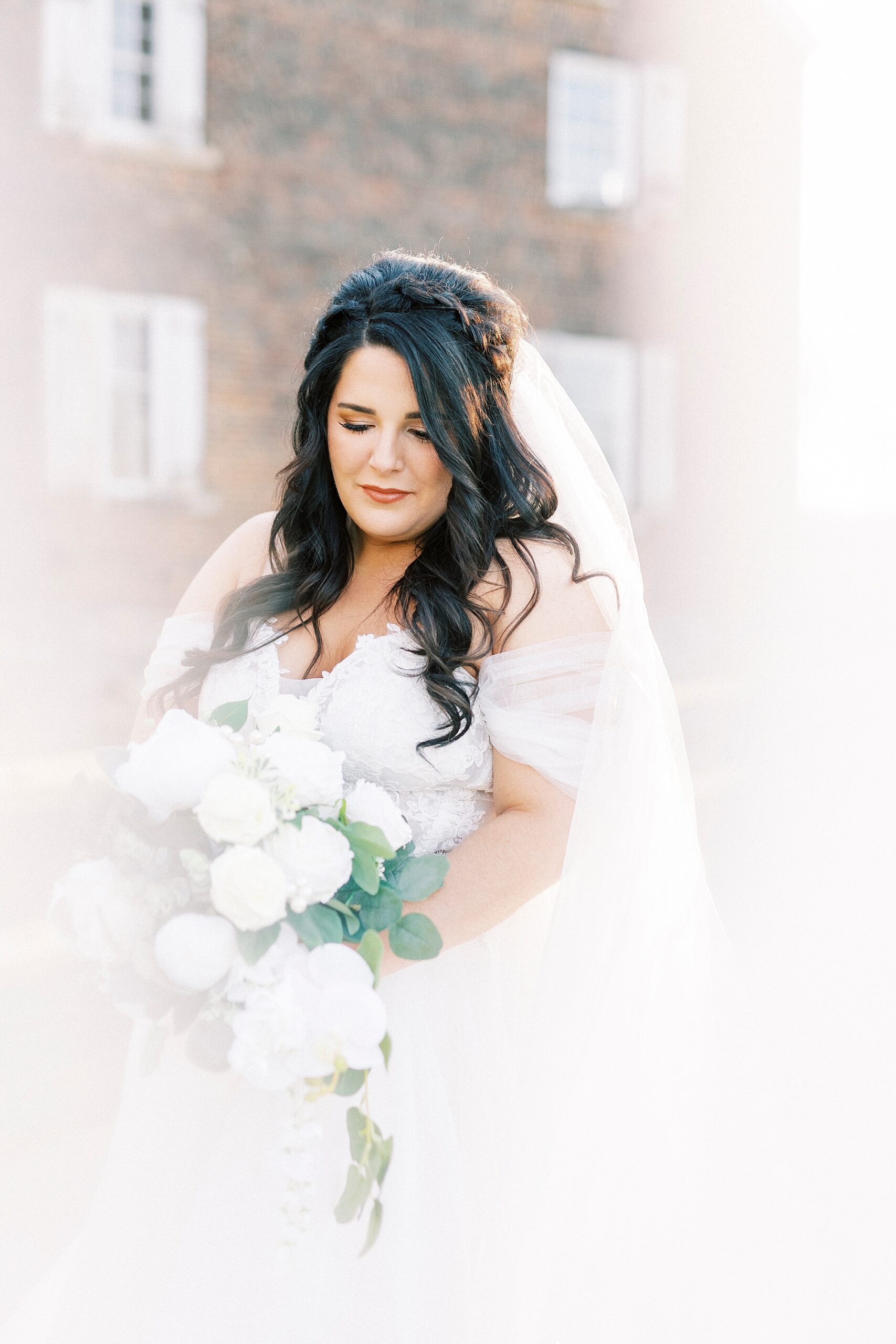 bride looks down at bouquet with veil around edge of photo 