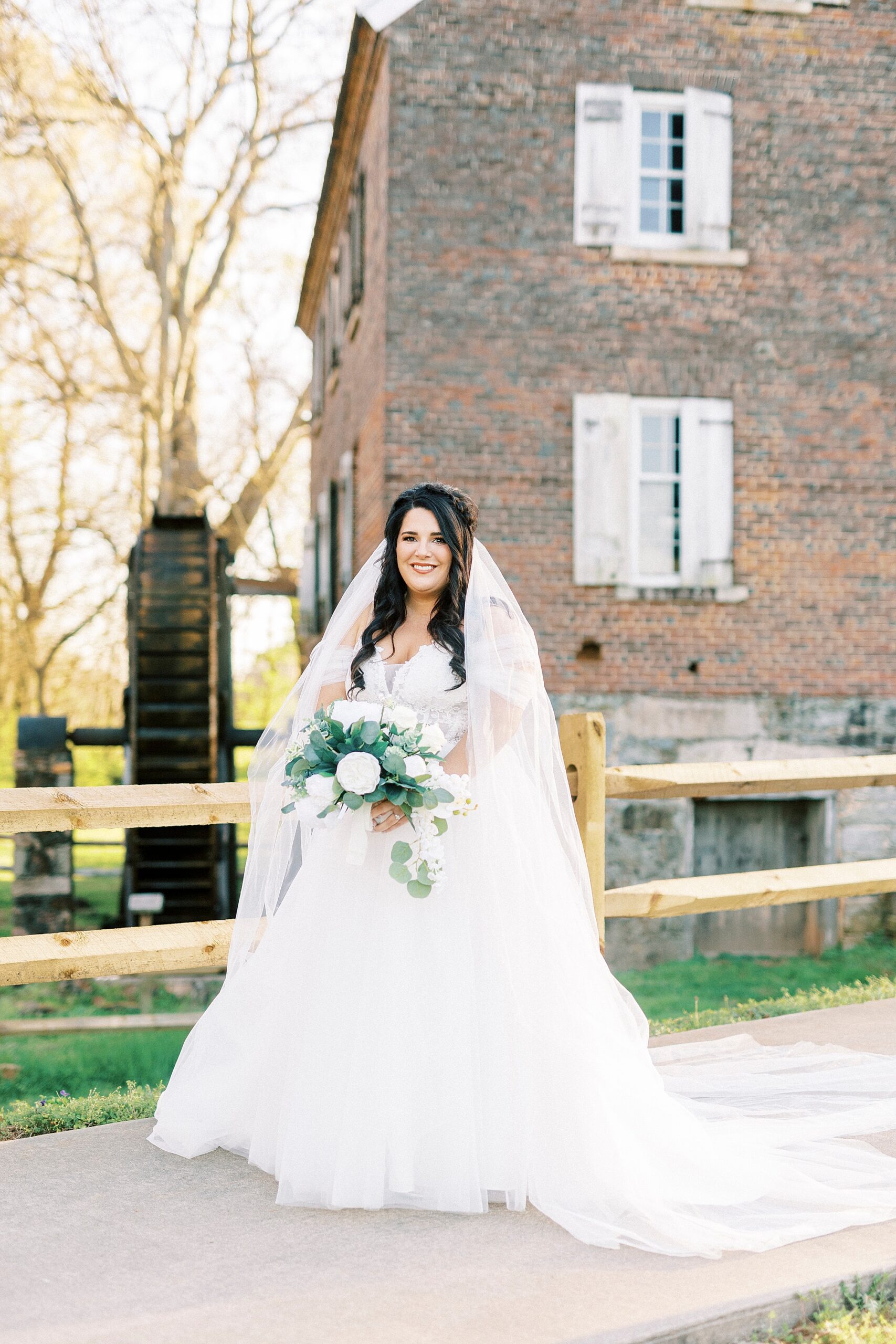 bride smiles holding bouquet of white flowers by brick building in Sloan Park