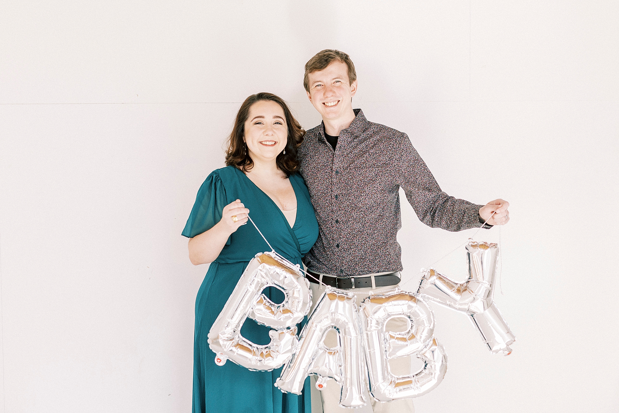expecting parents hold silver BABY sign during studio pregnancy announcement in Concord NC