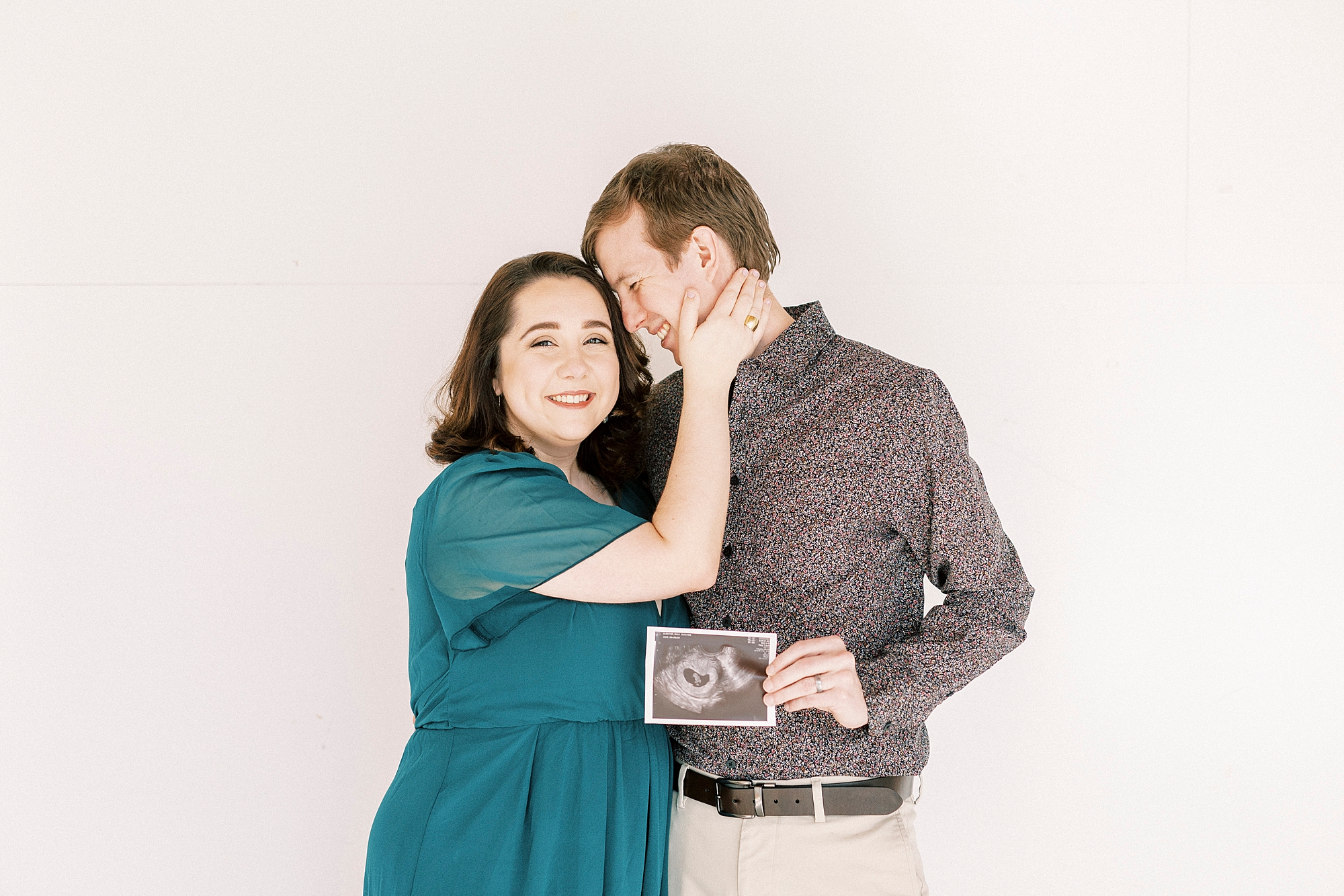 husband nuzzle wife's forehead during studio pregnancy announcement in Concord NC while holding sonogram 