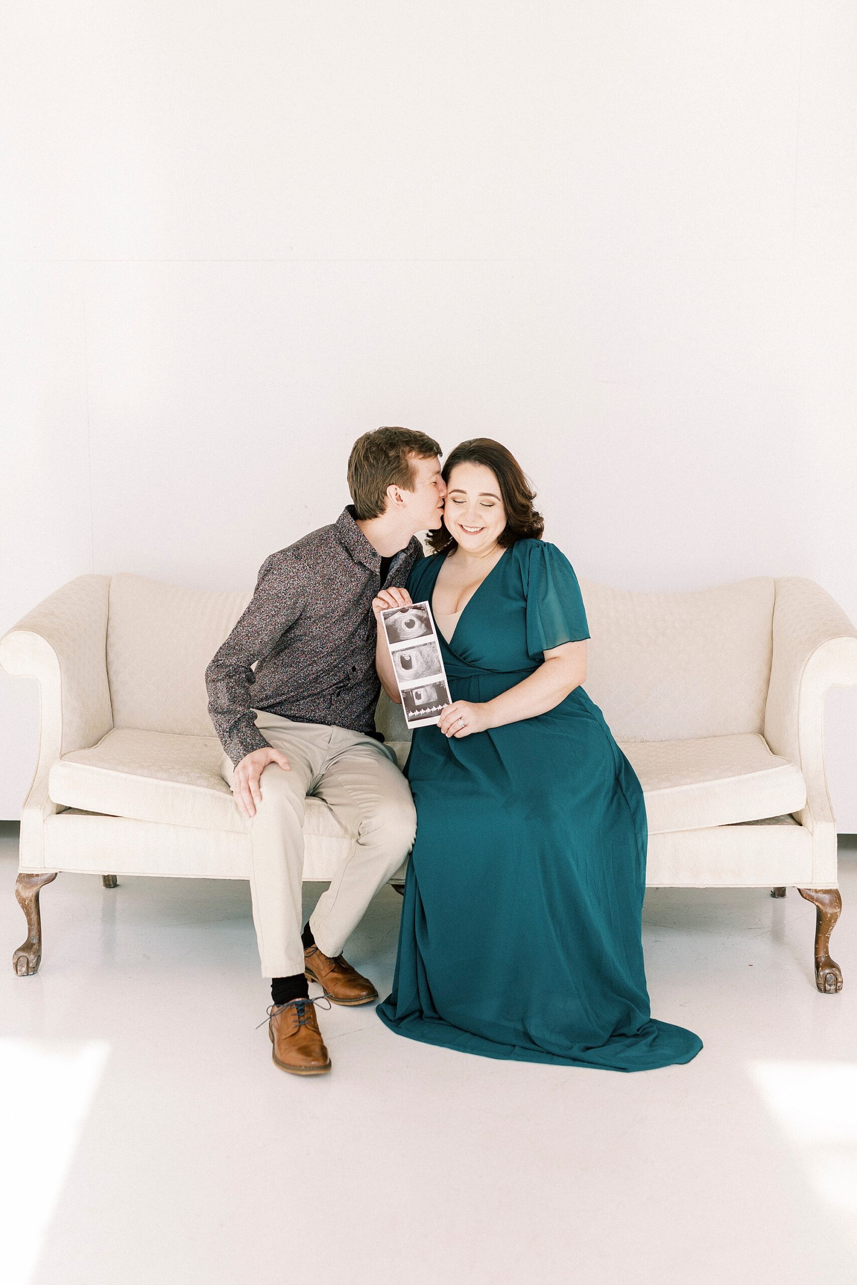 husband kisses wife's cheek during studio pregnancy announcement in Concord NC