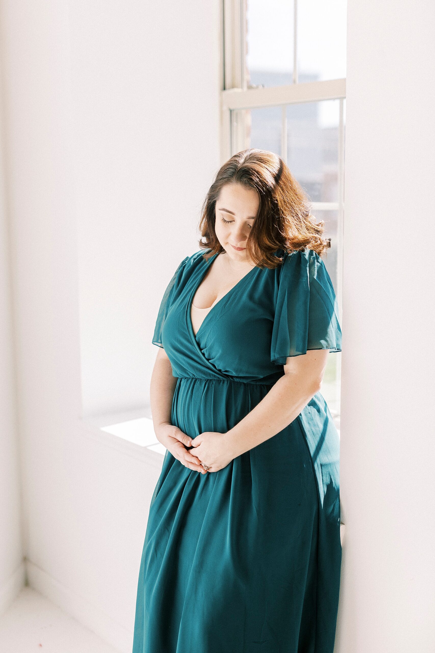 woman in teal gown holds baby bump looking down 