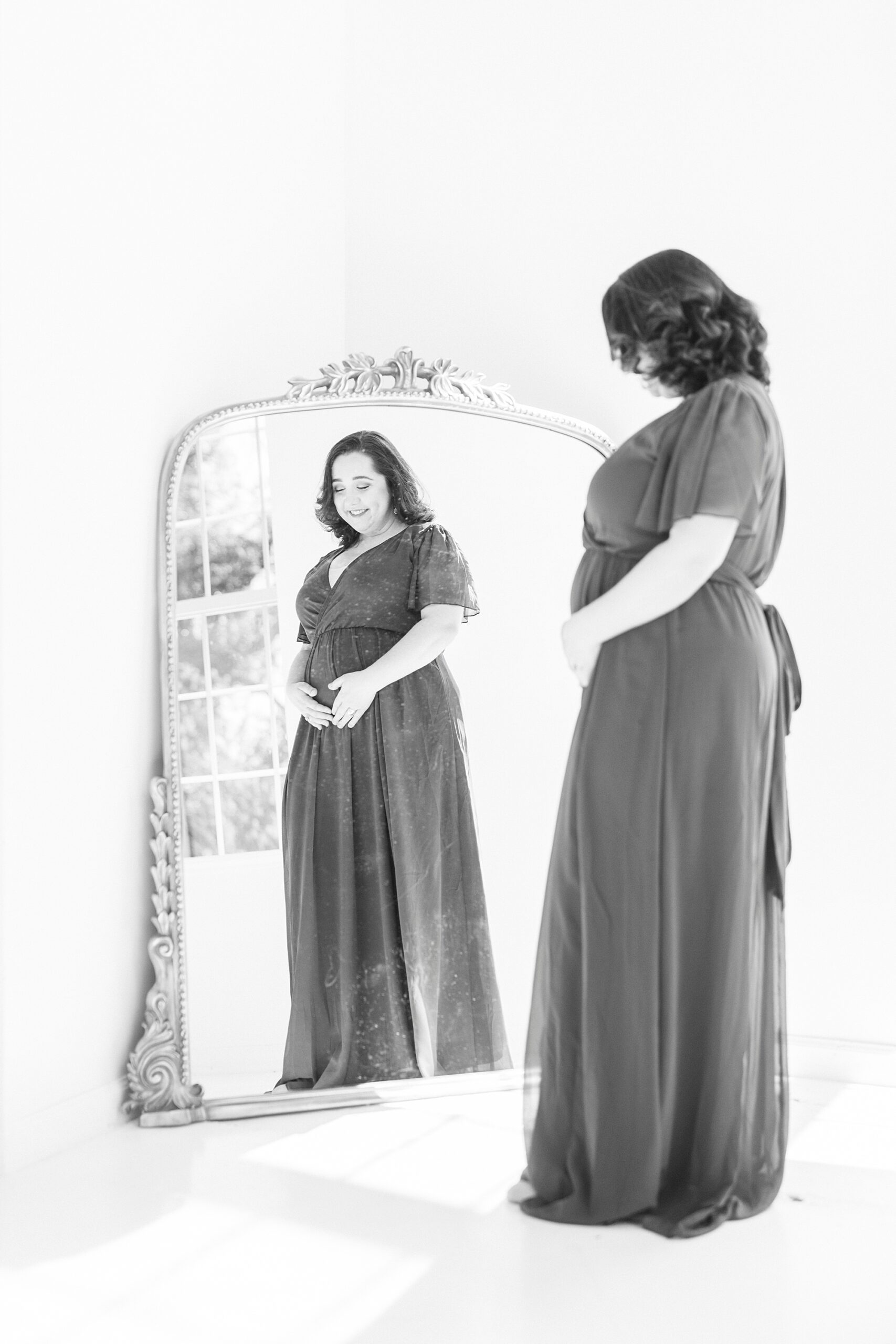 expecting mother holds baby bump looking at reflection in mirror 