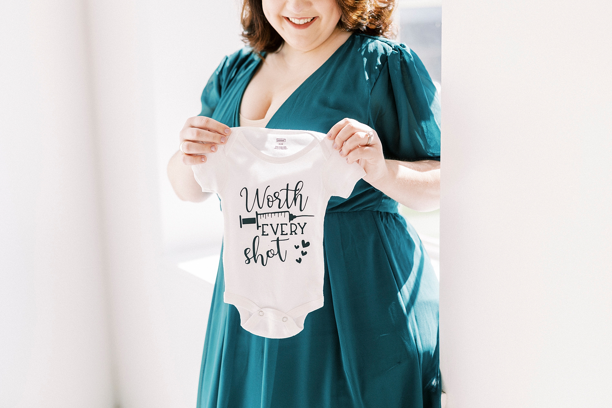 woman in teal gown holds IVF inspired onesie 