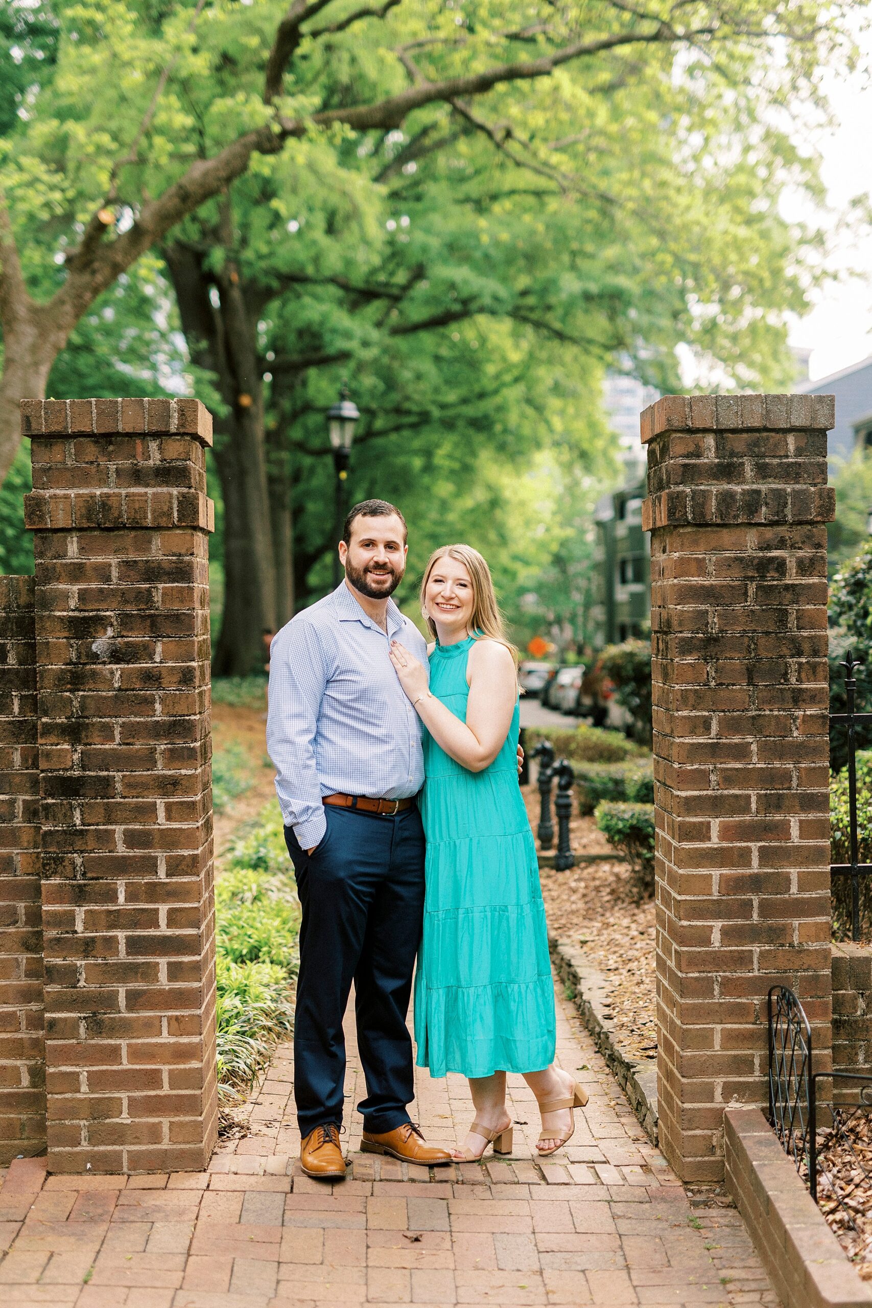 bride lays hand on groom's chest between brick pillars at Fourth Ward Park
