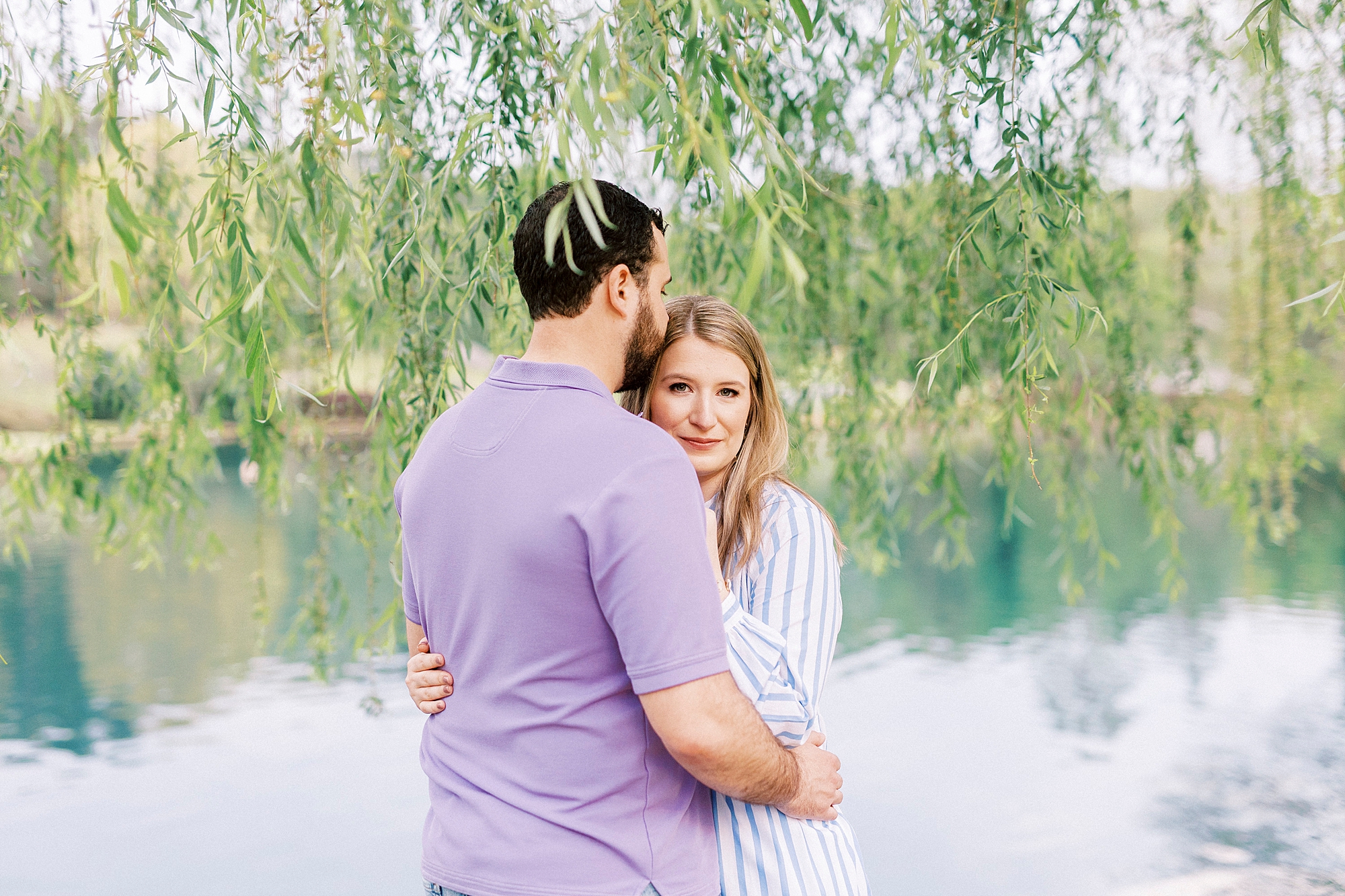 engaged couple hugs tightly under weeping willow at Freedom Park
