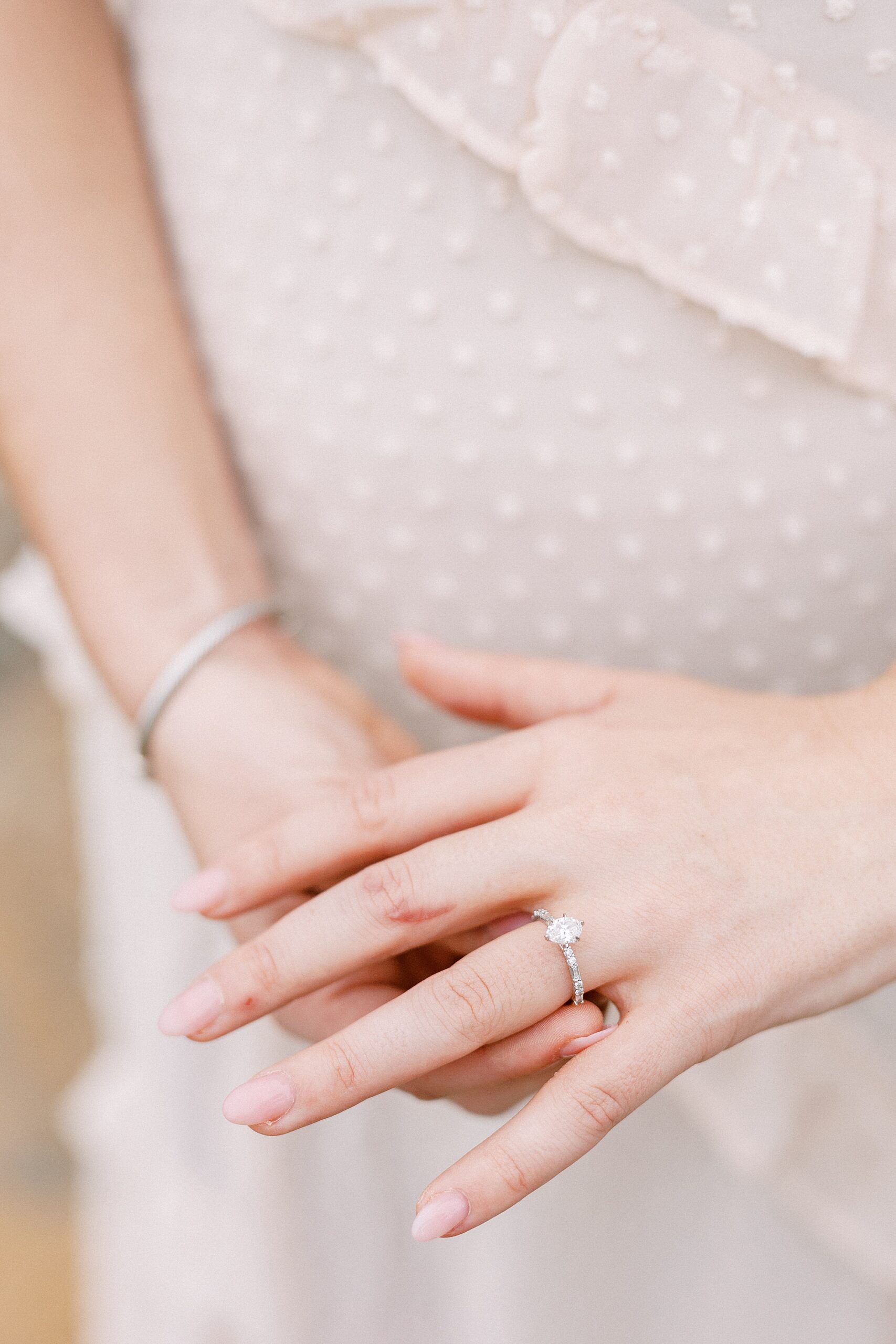woman shows off diamond ring in front off blush dress 