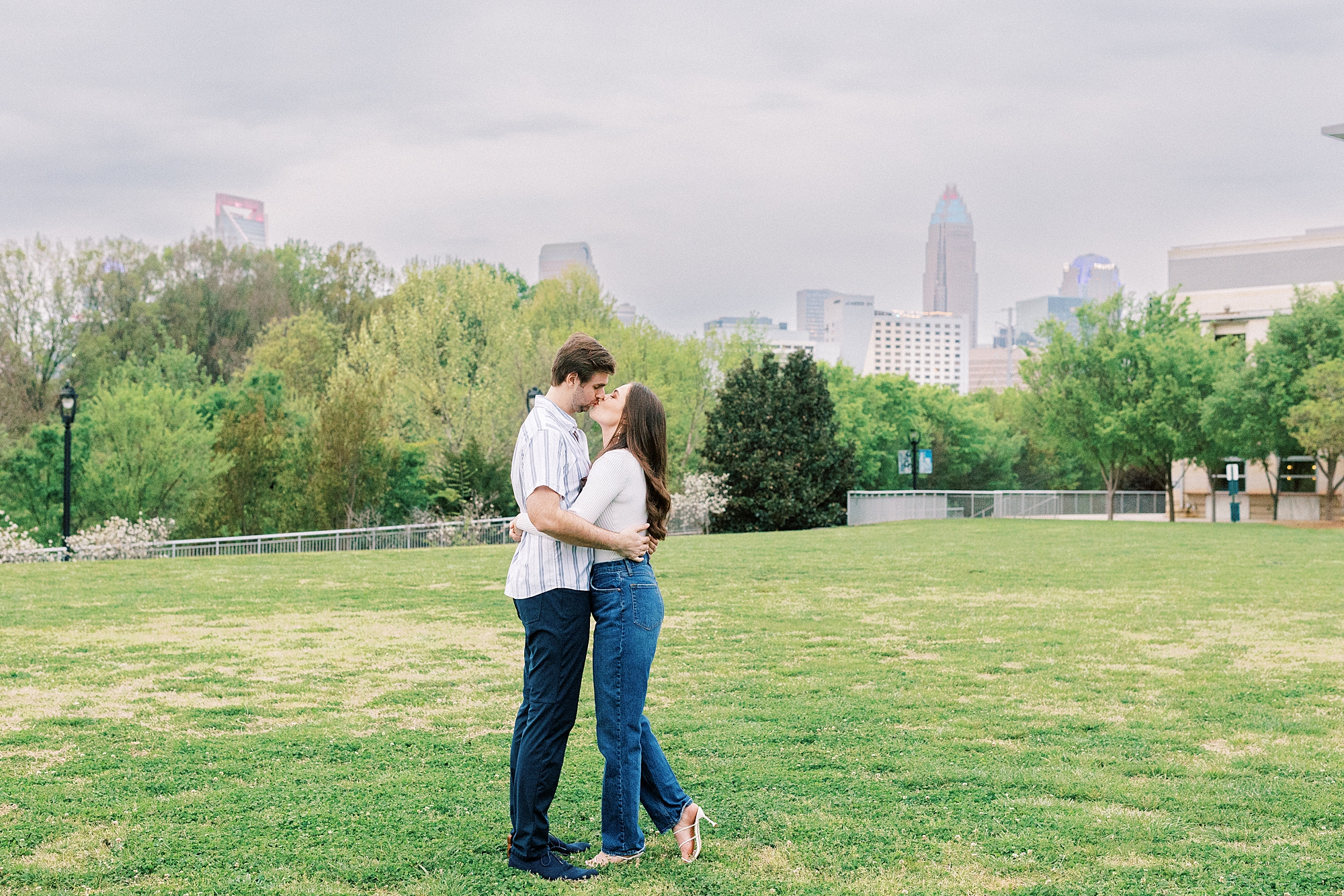 bride and groom kiss in park during engagement photos 