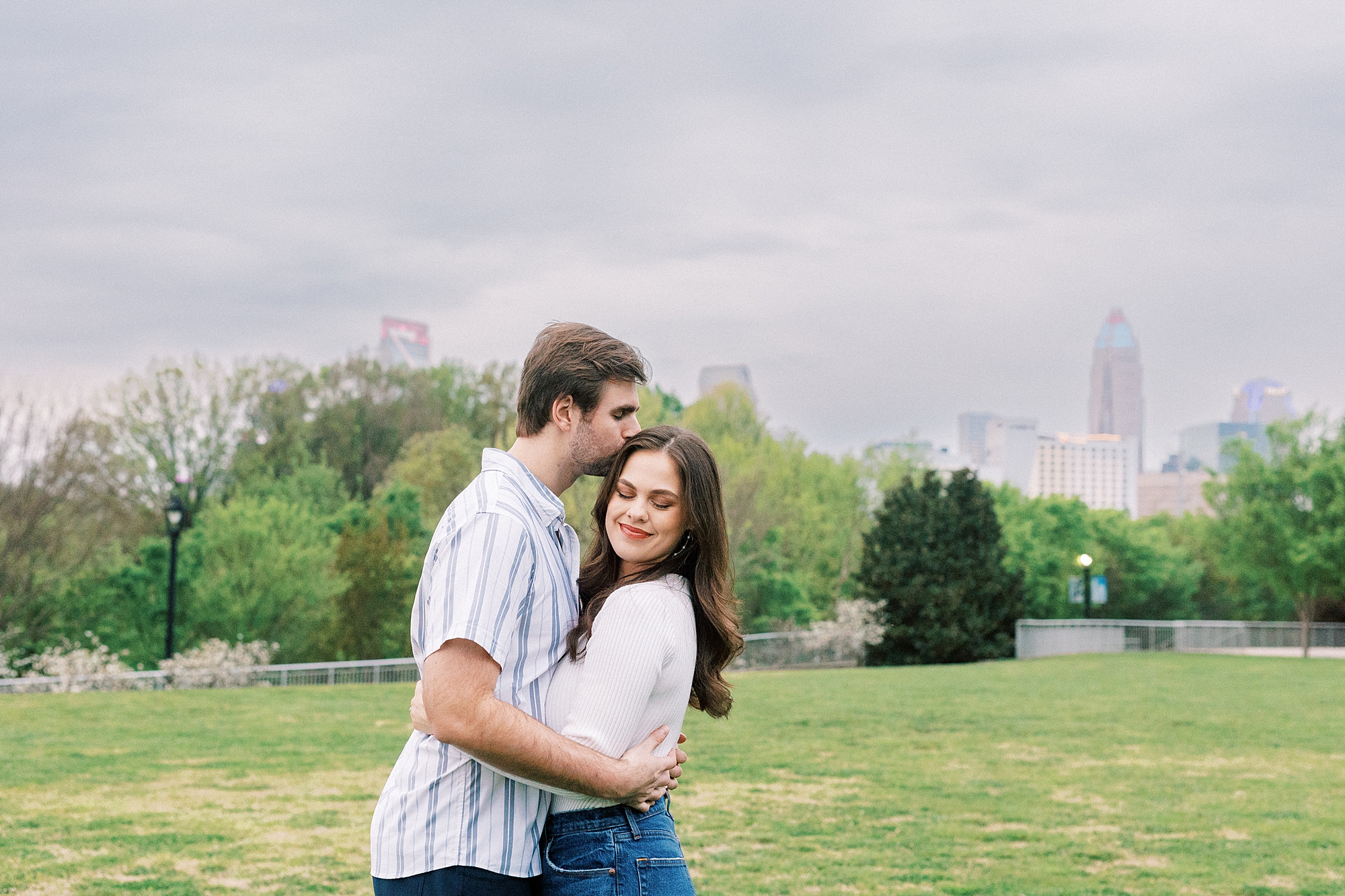 man kisses woman's forehead during engagement session at Midtown Park