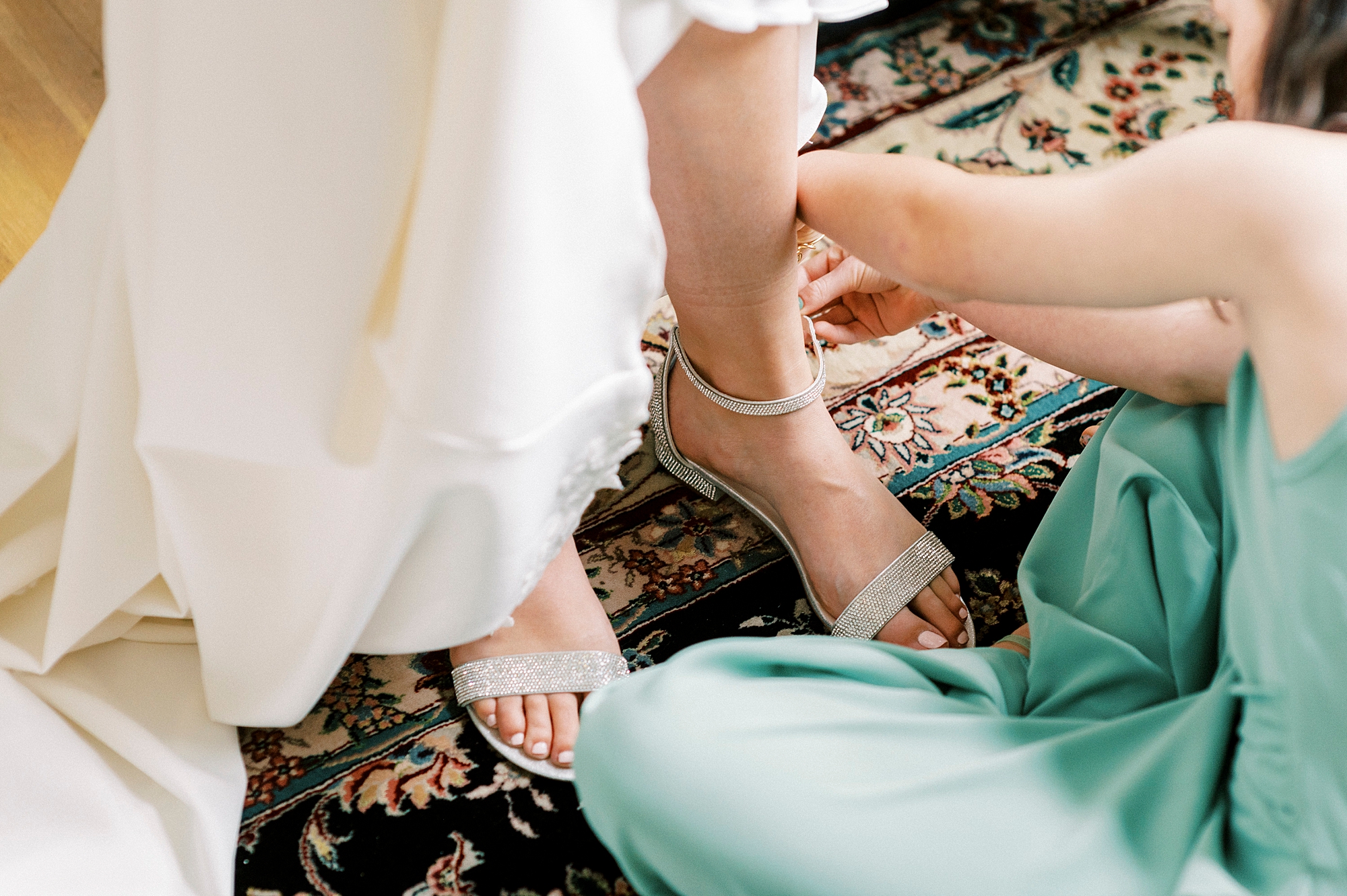 bridesmaid in green dress helps bride with buckle on shoes