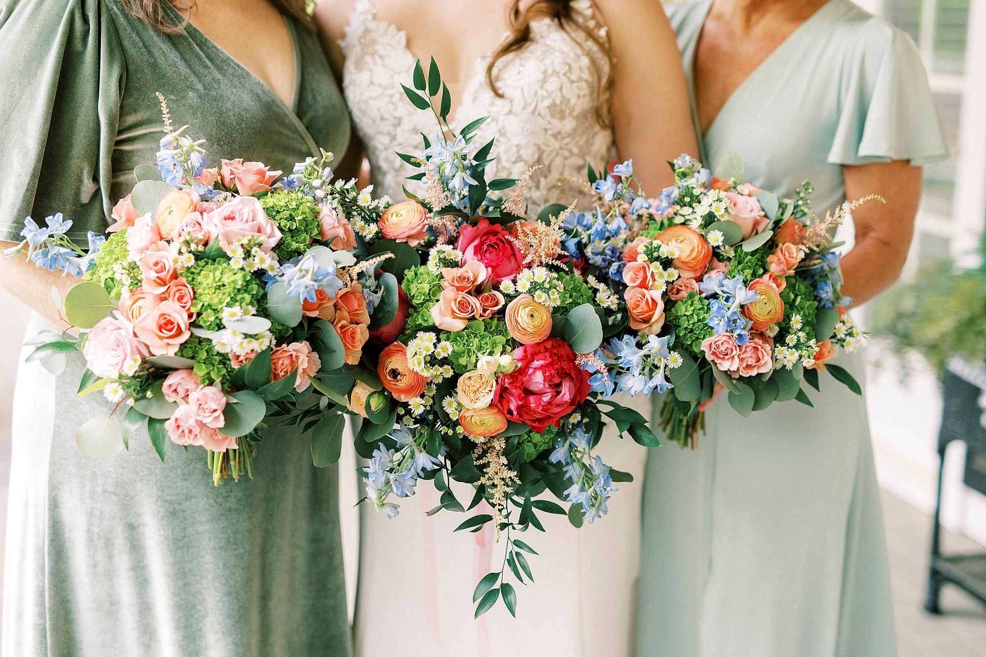 bride poses with bridesmaids in green gowns with bright bouquets 