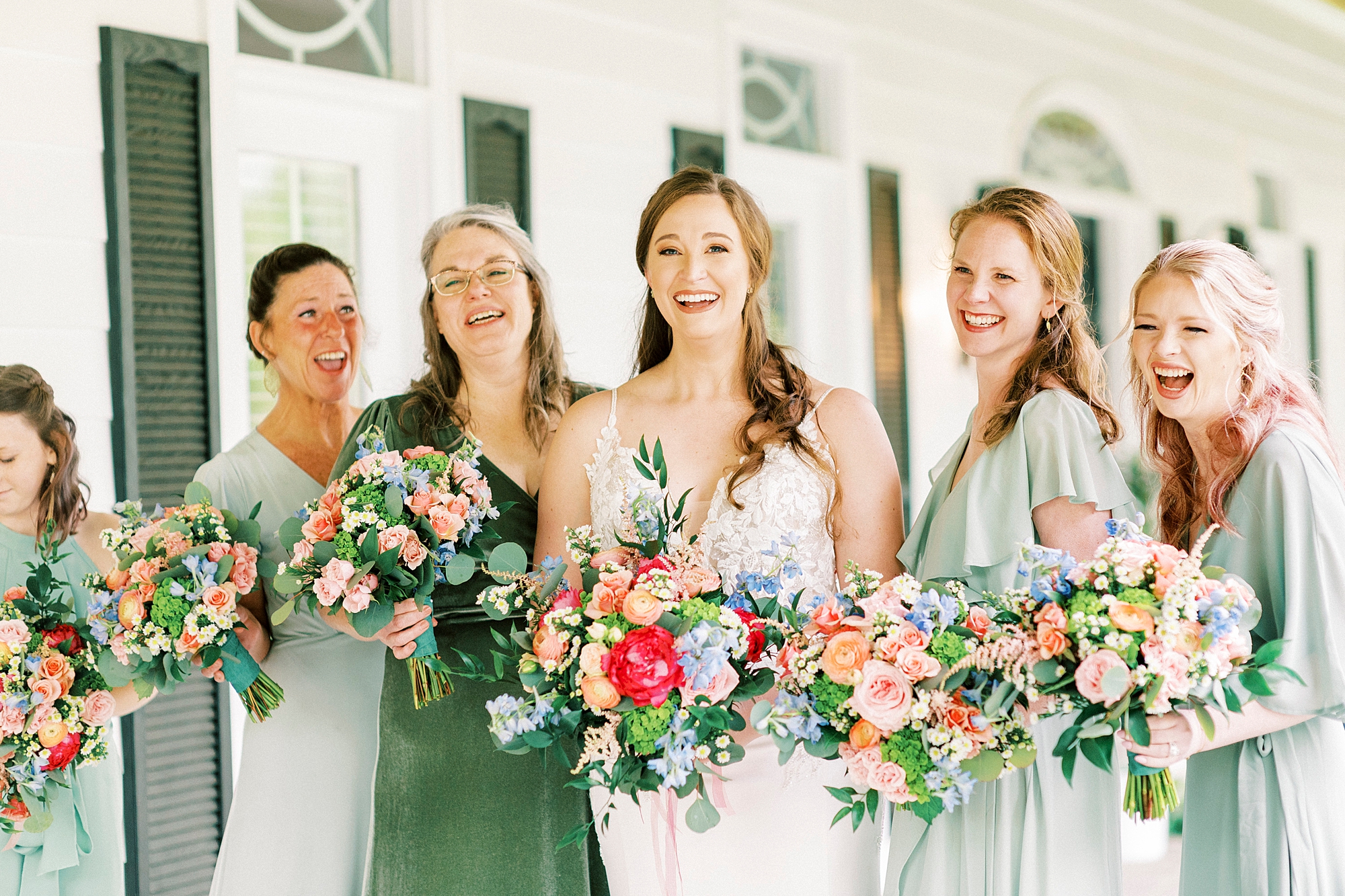 bride laughs with bridesmaids in mismatched green gowns on porch at The Saratoga Springs