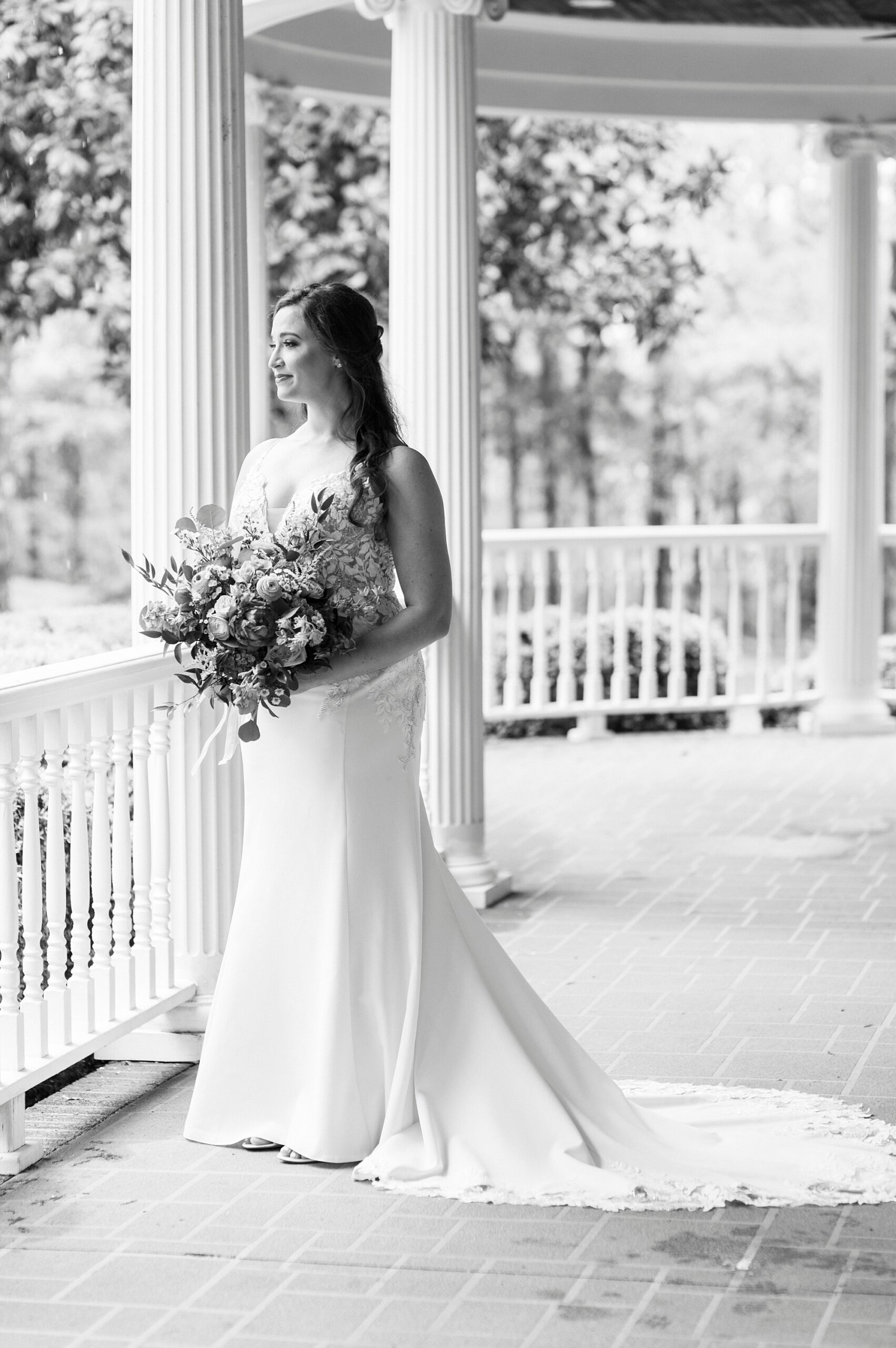 bride stands on porch holding bouquet and looking at yard at The Saratoga Springs