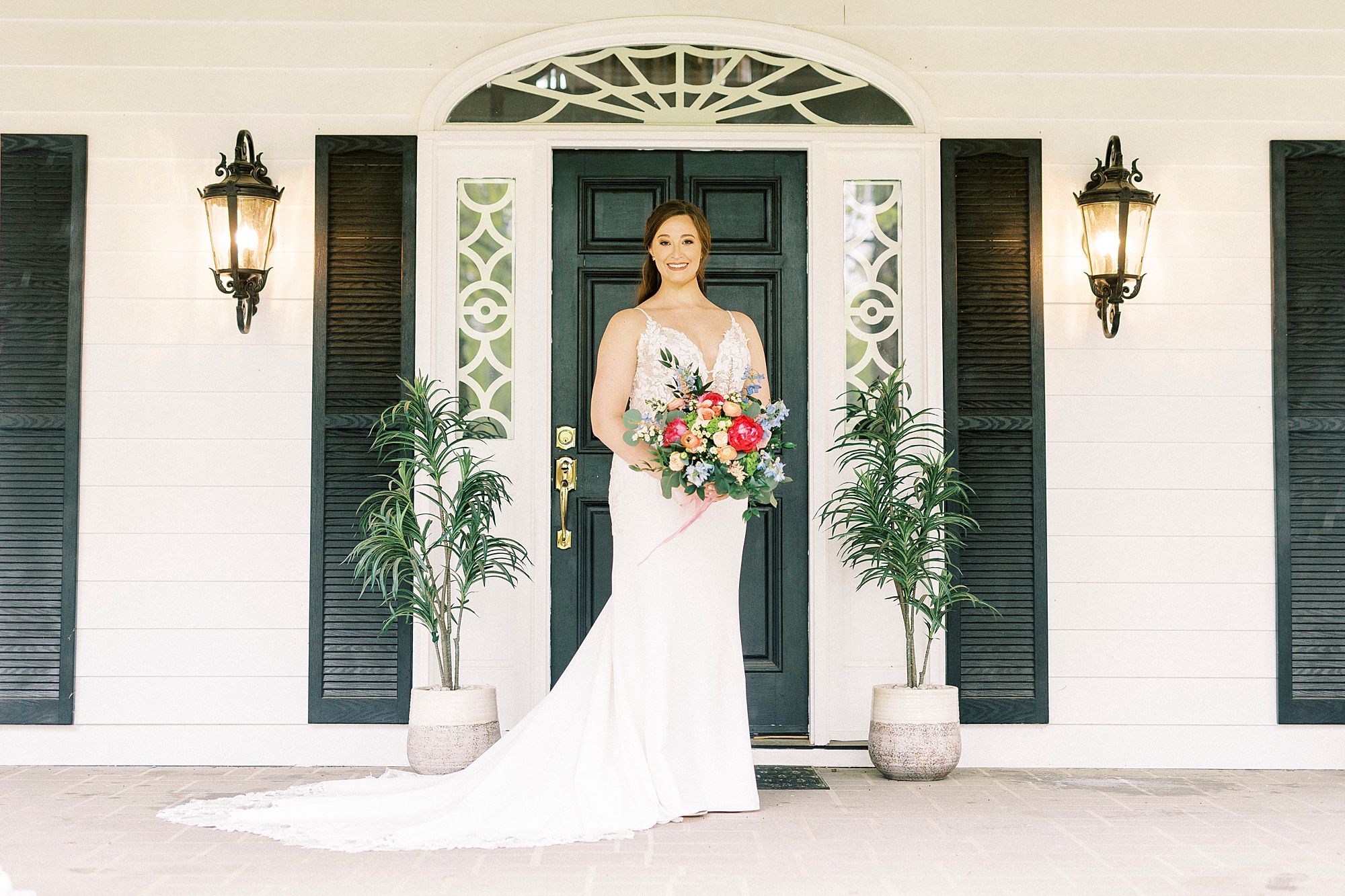 bride stands holding bouquet of bright flowers in front of green door at The Saratoga Springs