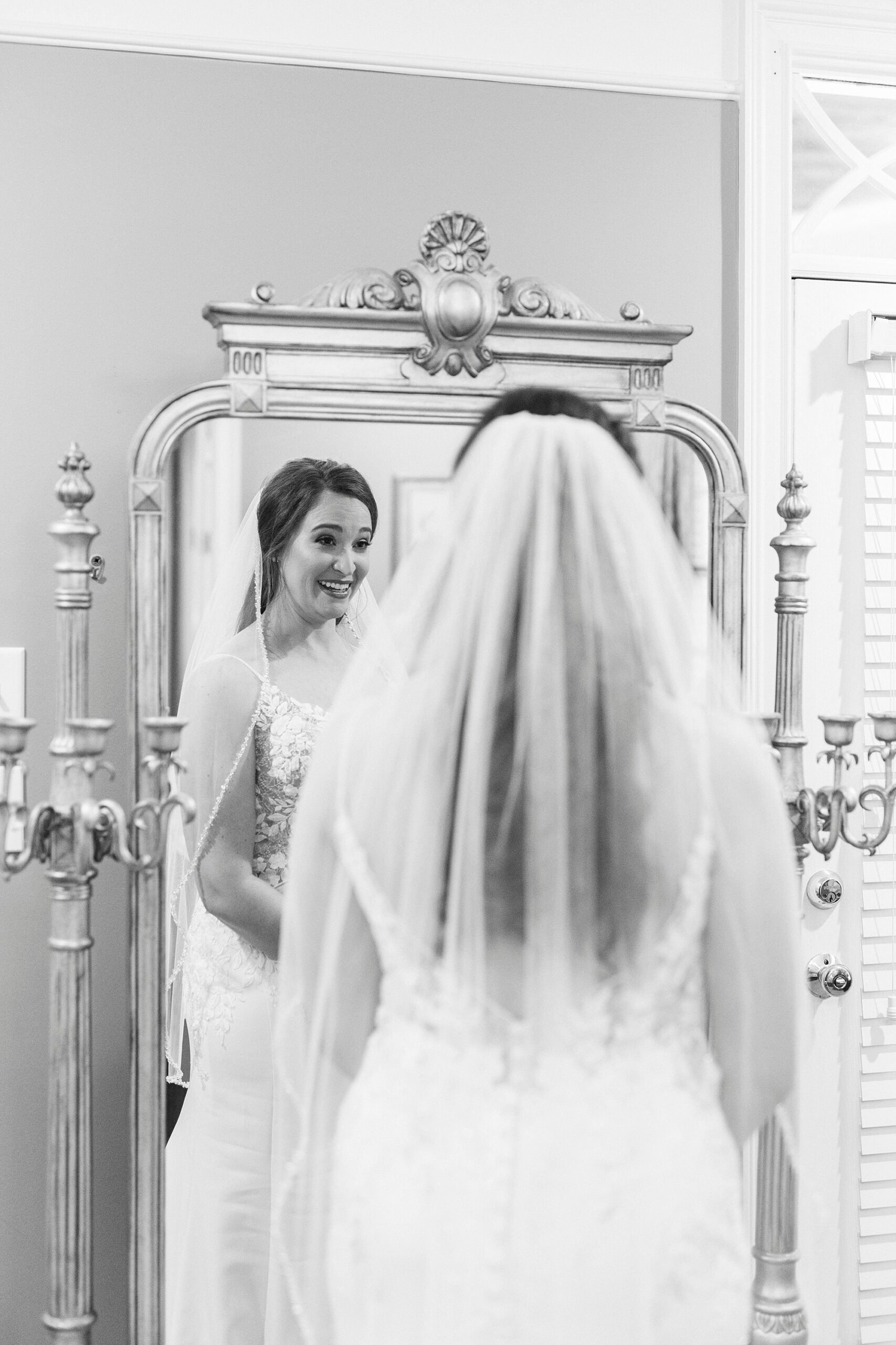 bride looks in mirror with veil on head in wedding gown 