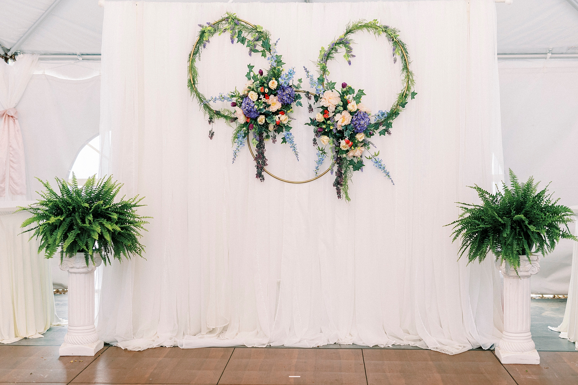 greenery covered hoops hang on white backdrop at The Saratoga Springs