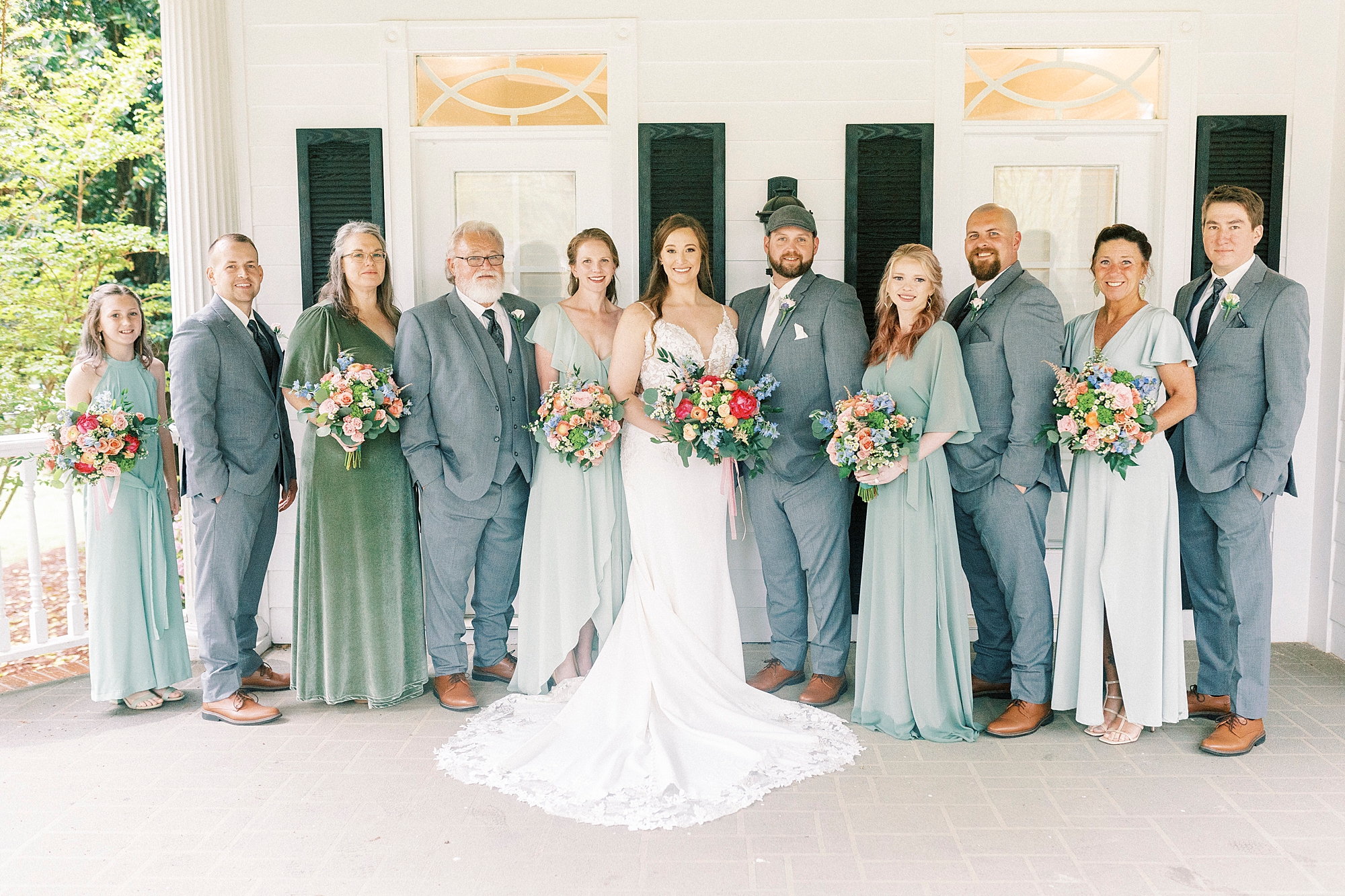 bride and groom stand with wedding party in green dresses and grey suits 