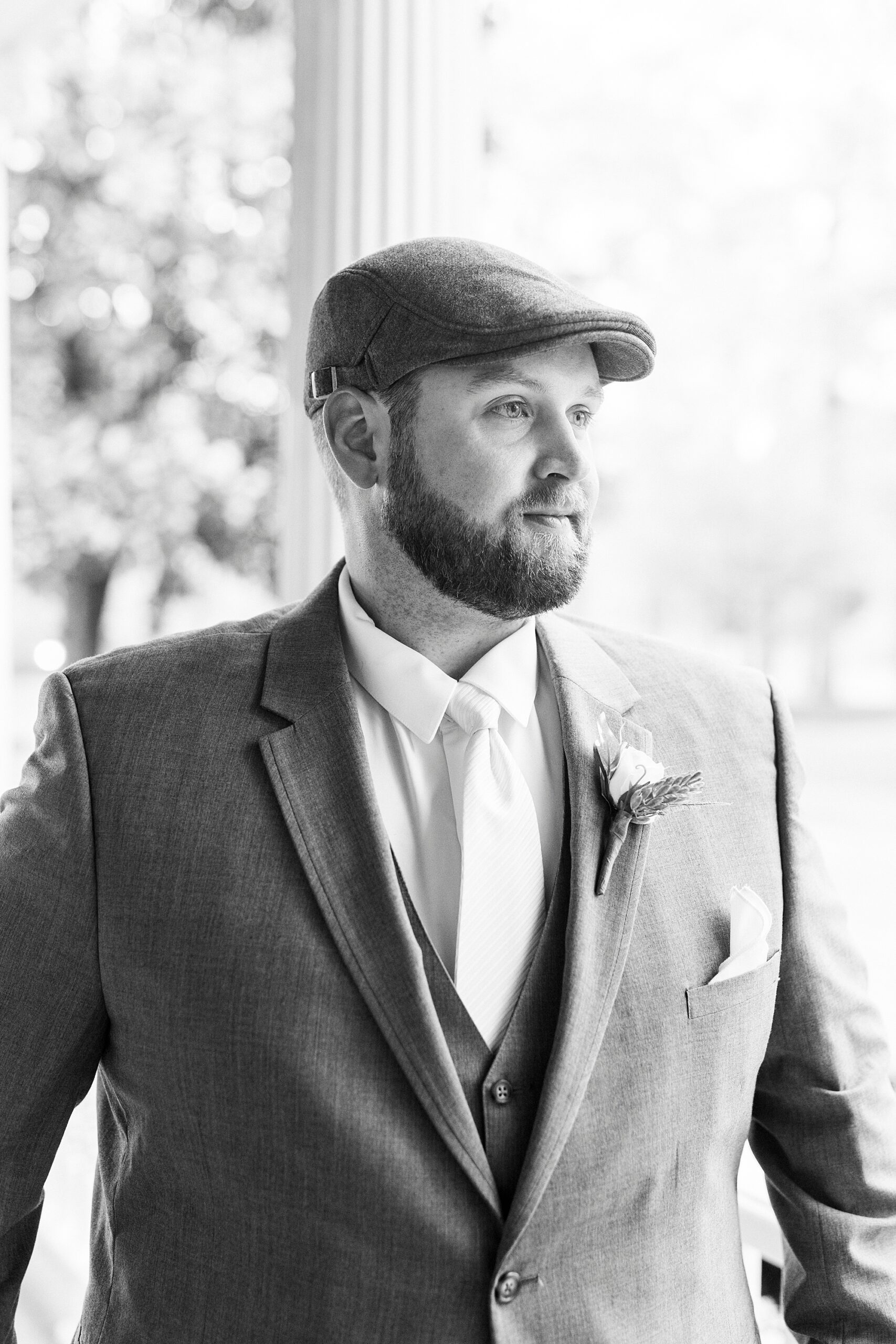 groom in suit with newsboy hat stands on porch 