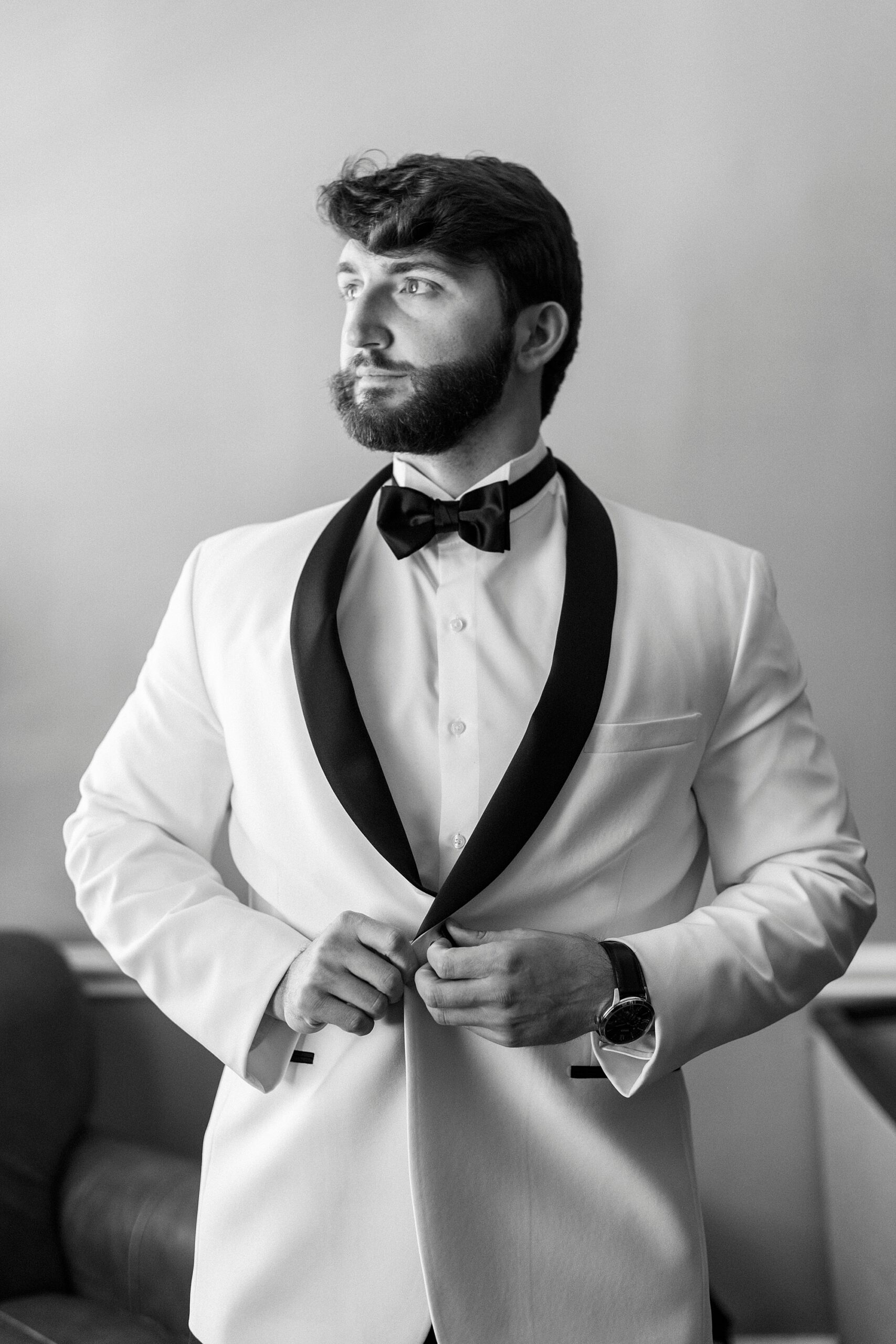 groom adjusts buttons on white tux jacket 