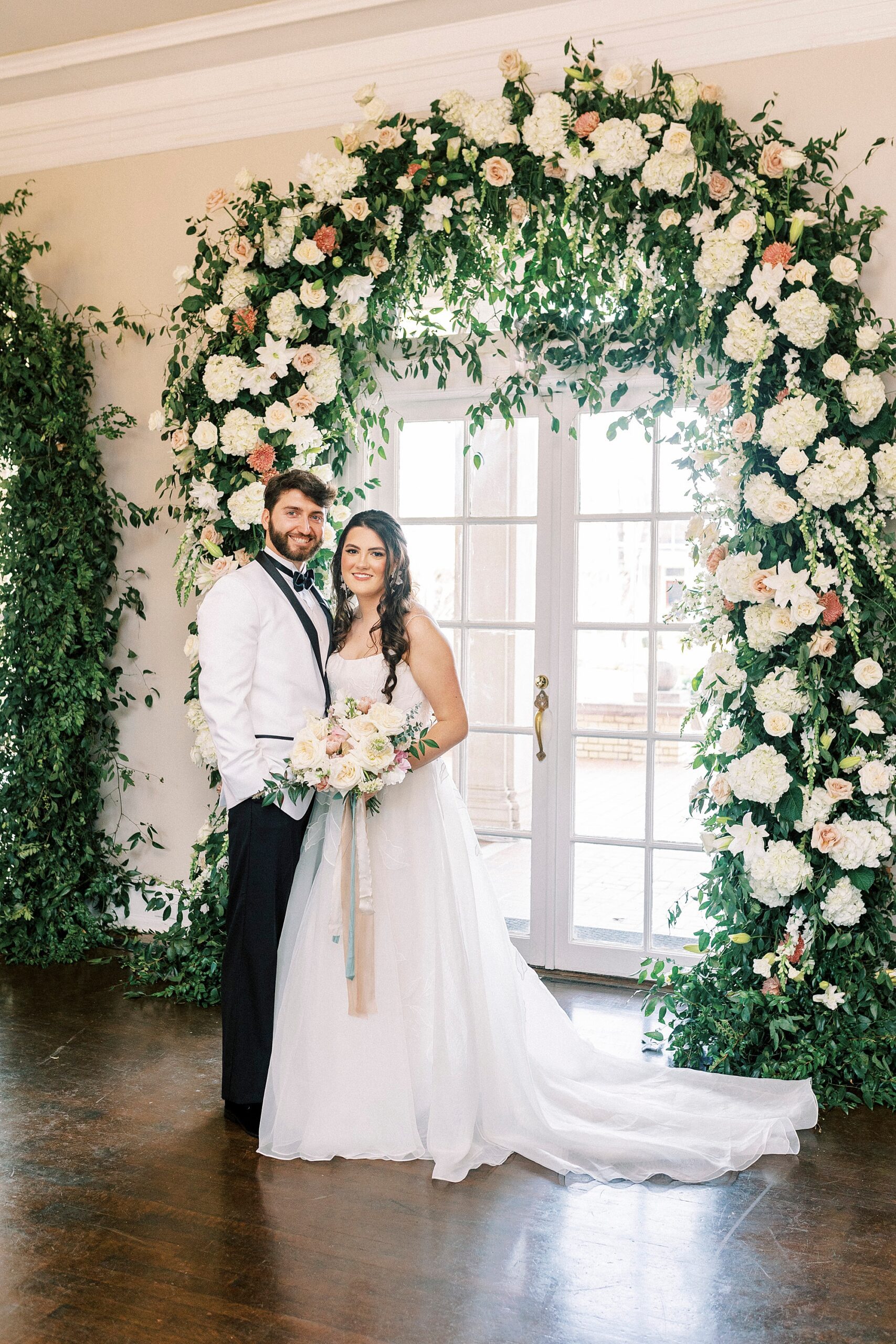 bride and groom hug under arbor with white and peach roses 