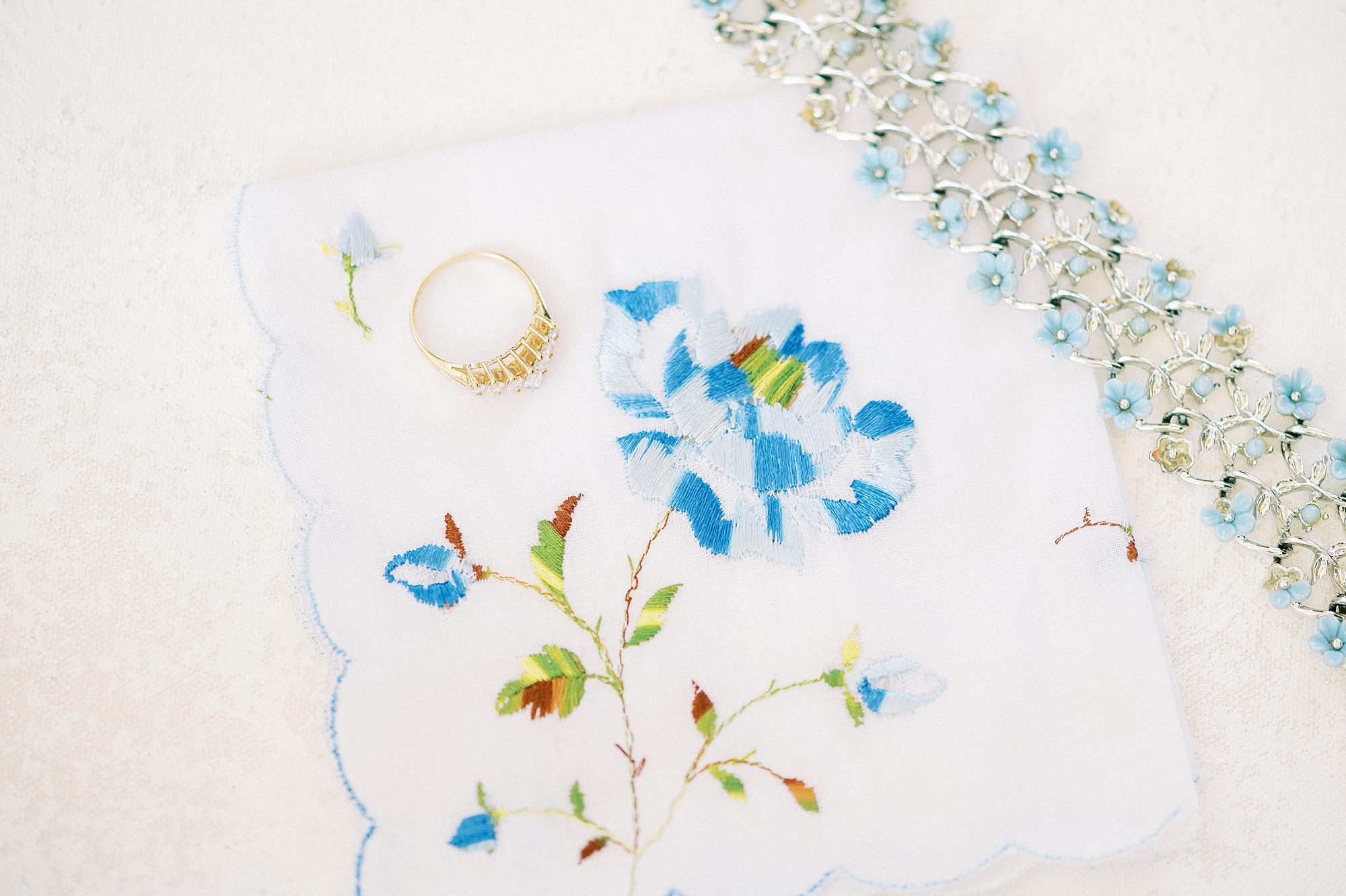 bride's wedding ring lays on kerchief with blue flower 