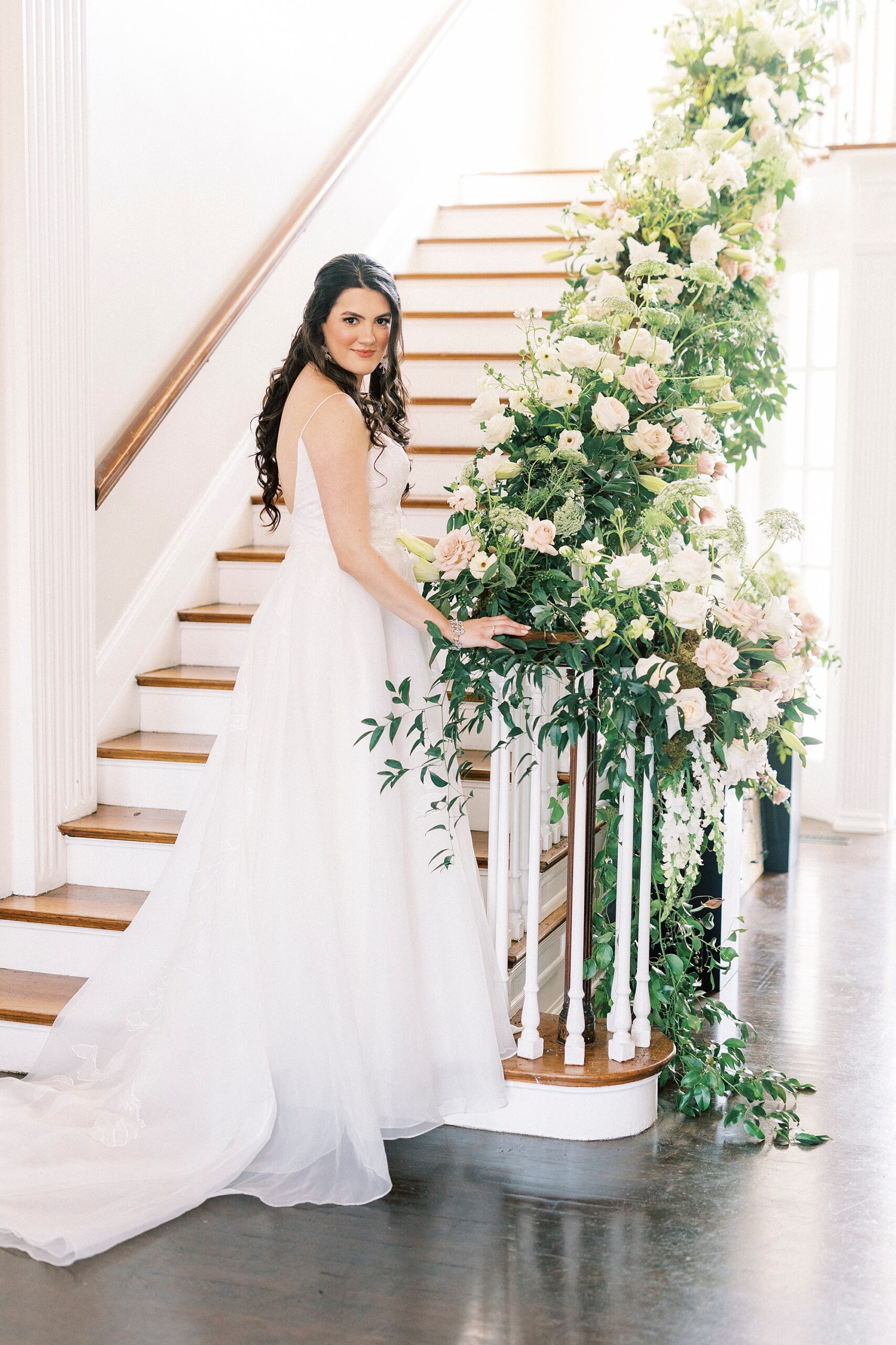 bride stands on staircase with greenery and roses on banister 
