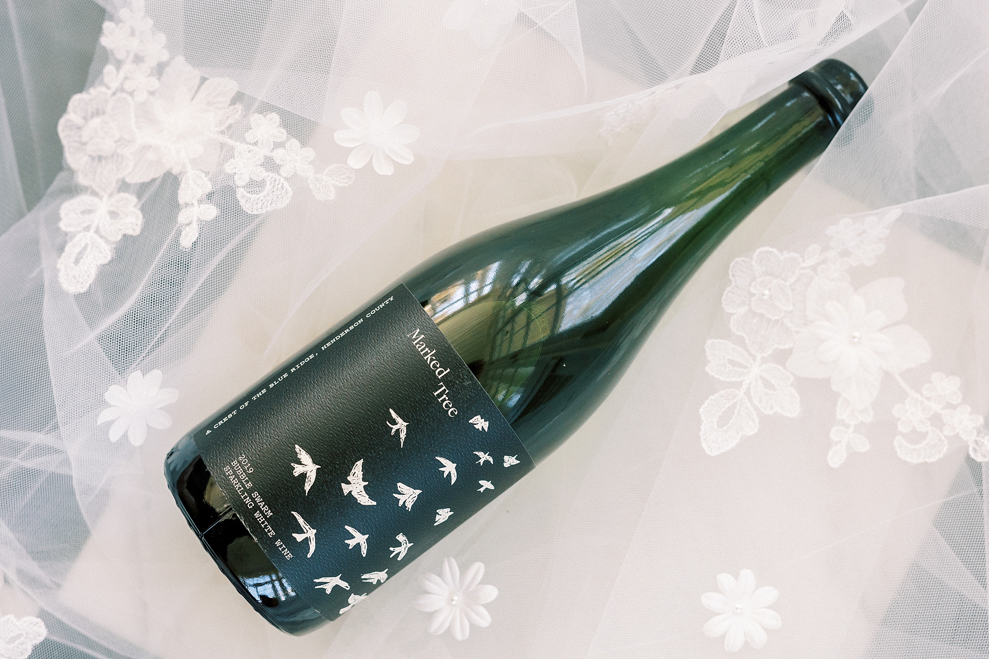 champagne bottle lays on veil with floral accents 