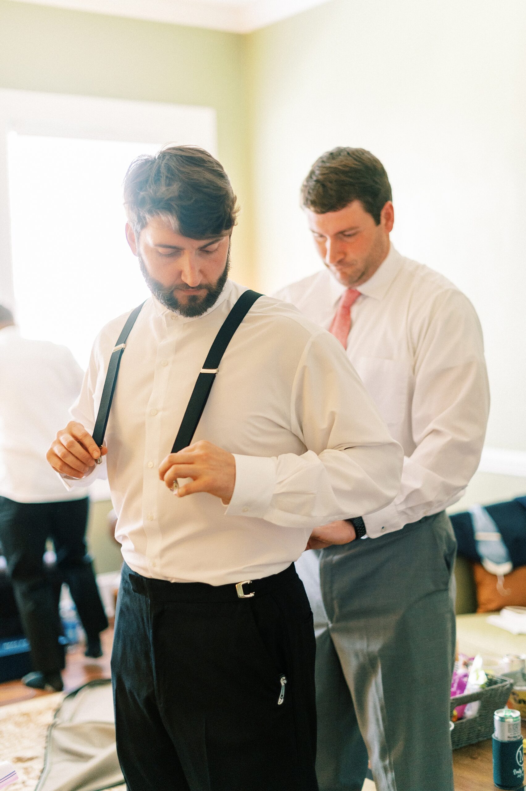 groomsman helps groom adjust suspenders before wedding 