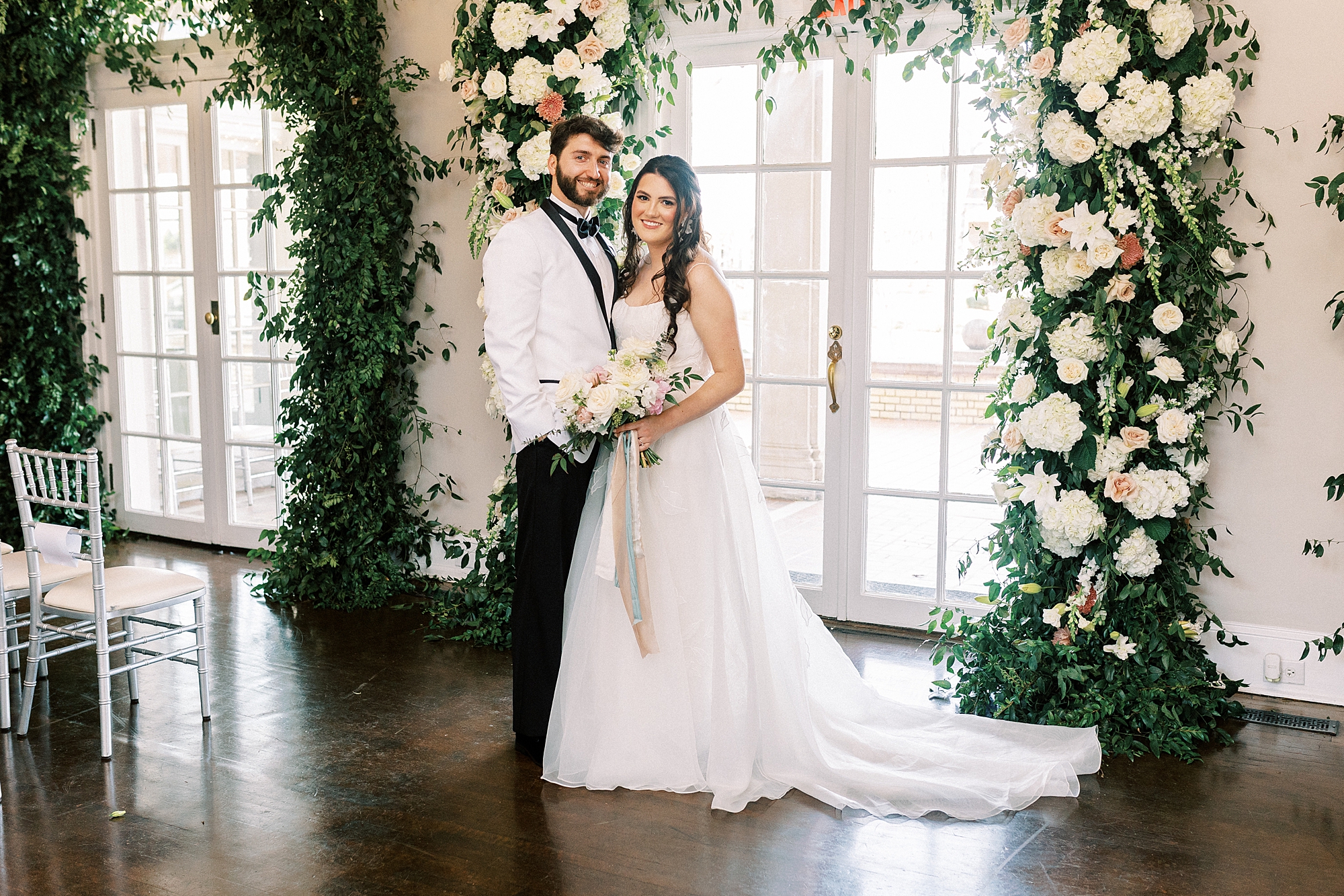 newlyweds hug by floral arbor inside Separk Mansion