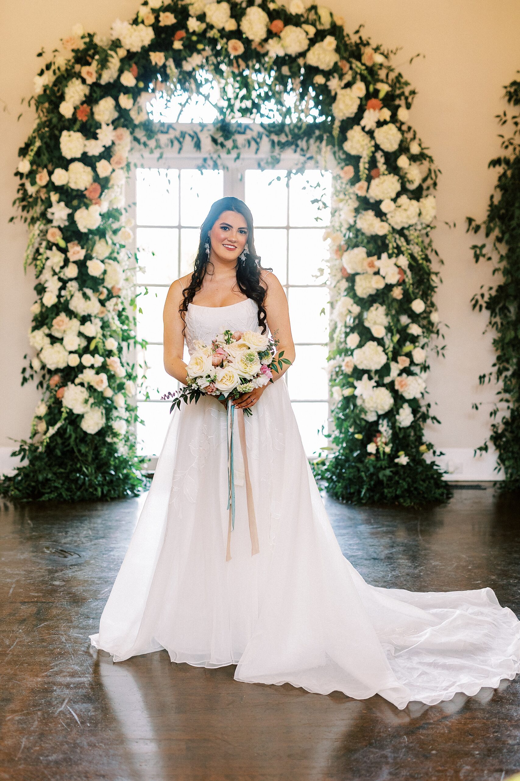 bride stands under arbor with ivory flowers at Separk Mansion