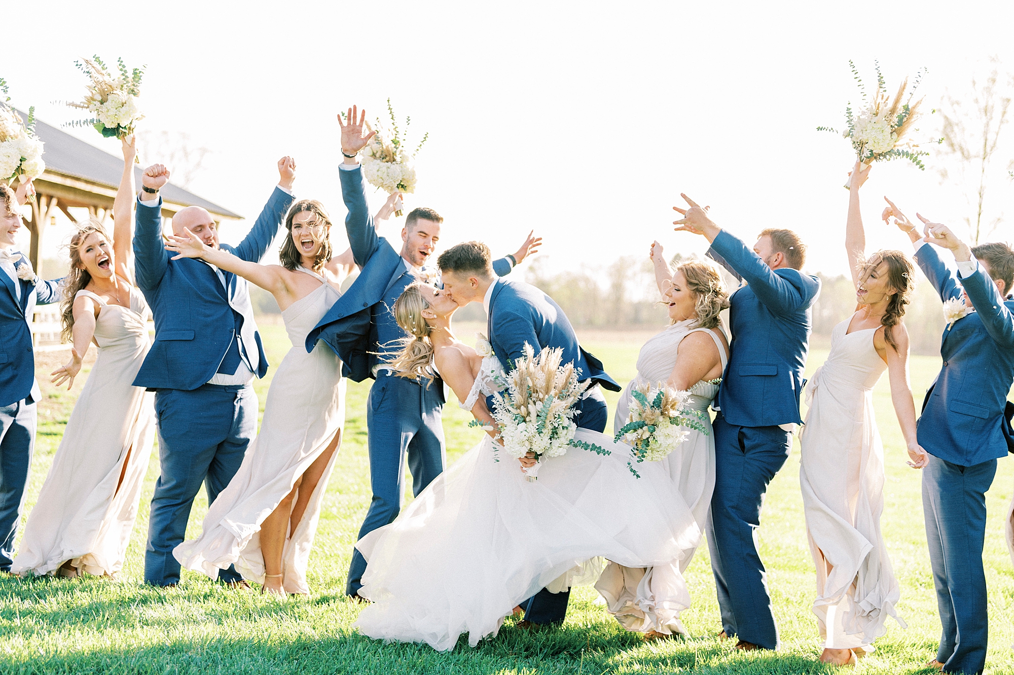 newlyweds kiss while bride and groom cheer at the Farmstead