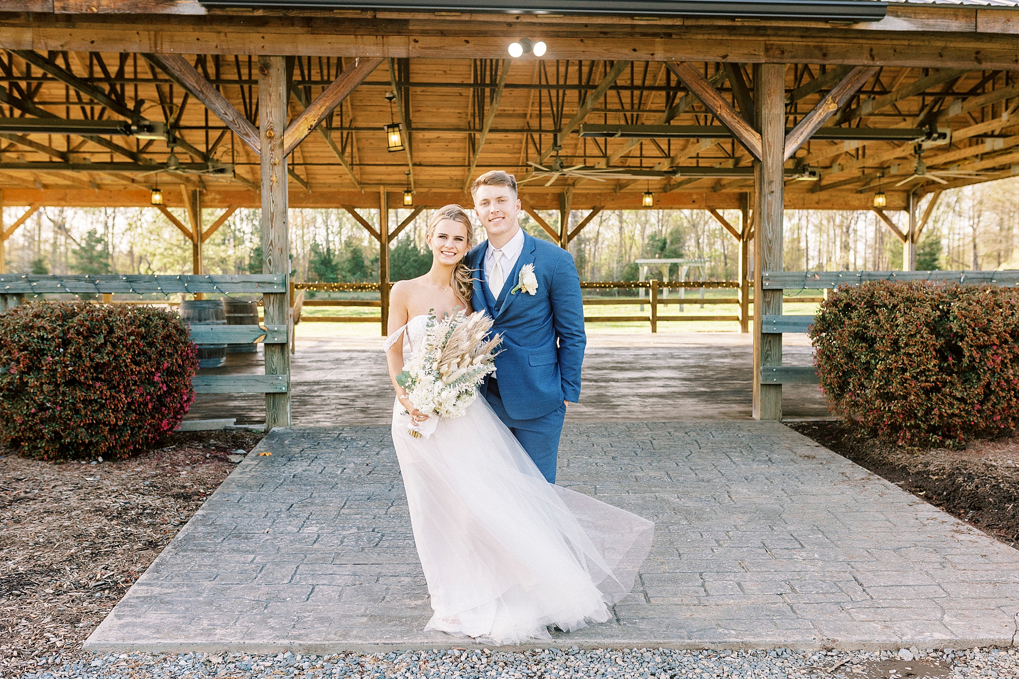 bride and groom stand outside wooden structure at the Farmstead