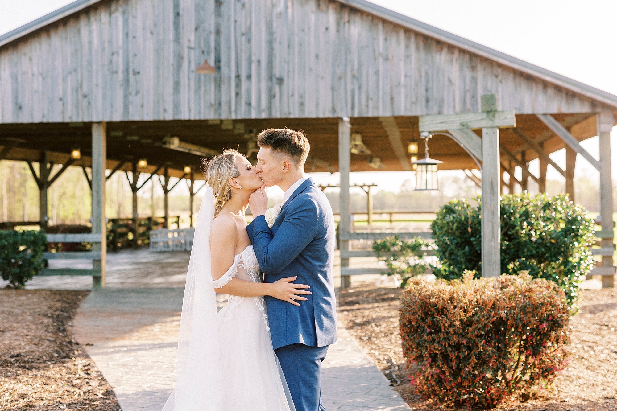 newlyweds kiss near wooden structure at the Farmstead