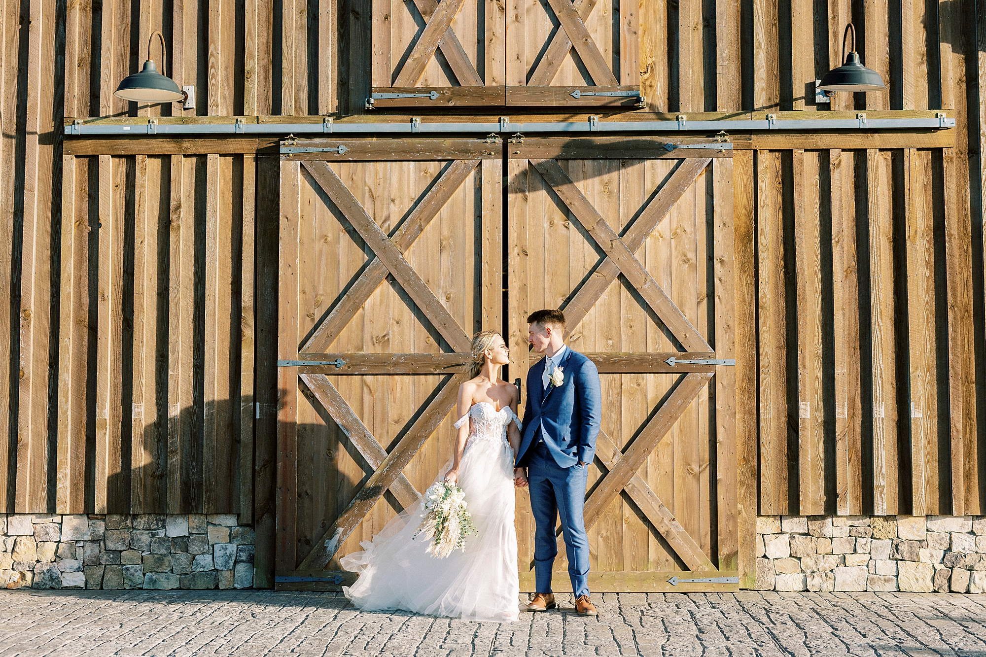 bride and groom lean against wooden barn door at the Farmstead