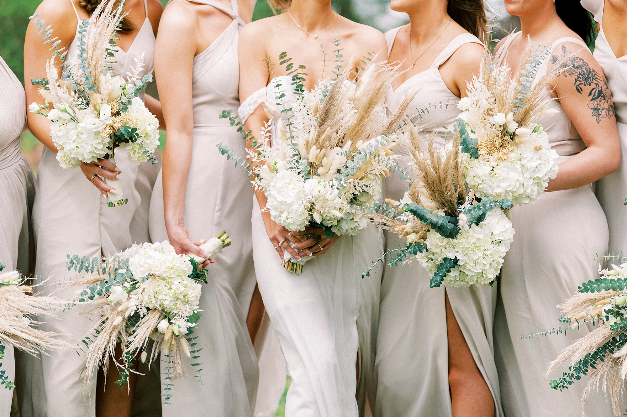 bride and bridesmaids hold bouquets of white and green flowers with cattails 
