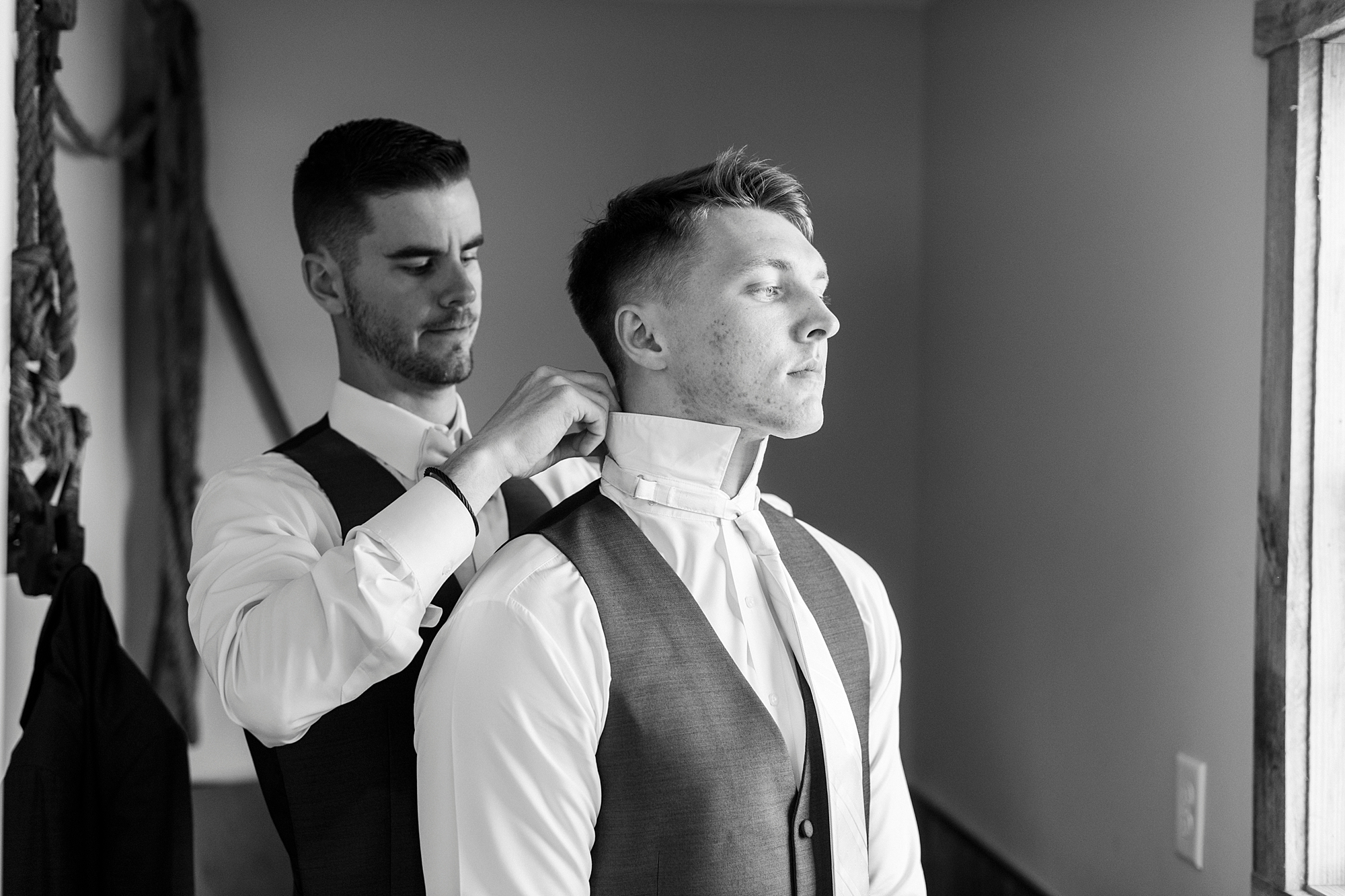 groomsman helps groom with buttons and tie