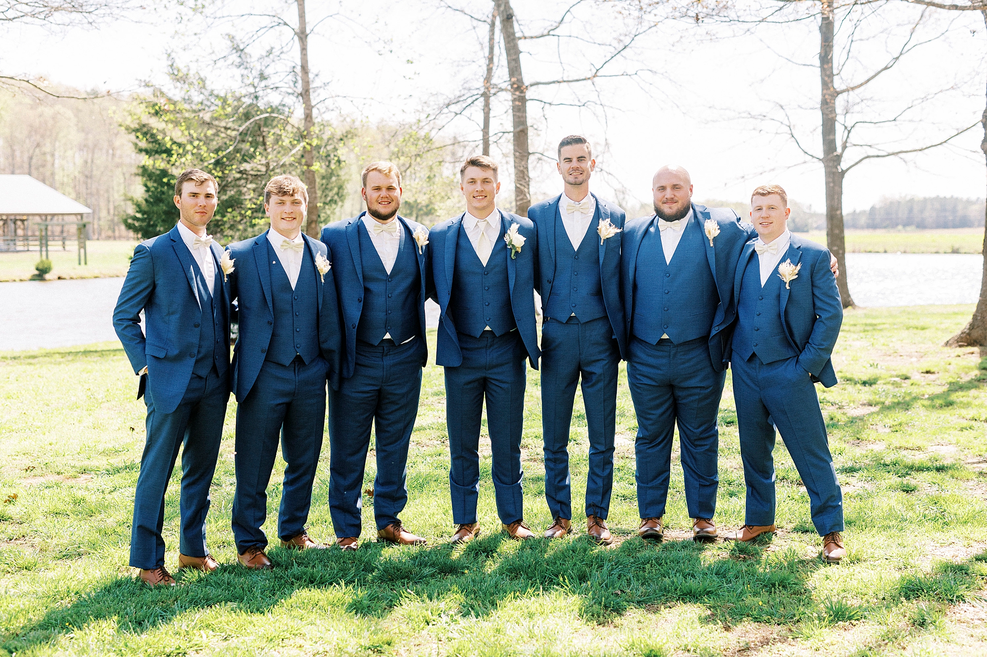 groom and groomsmen in navy suits stand together at The Farmstead