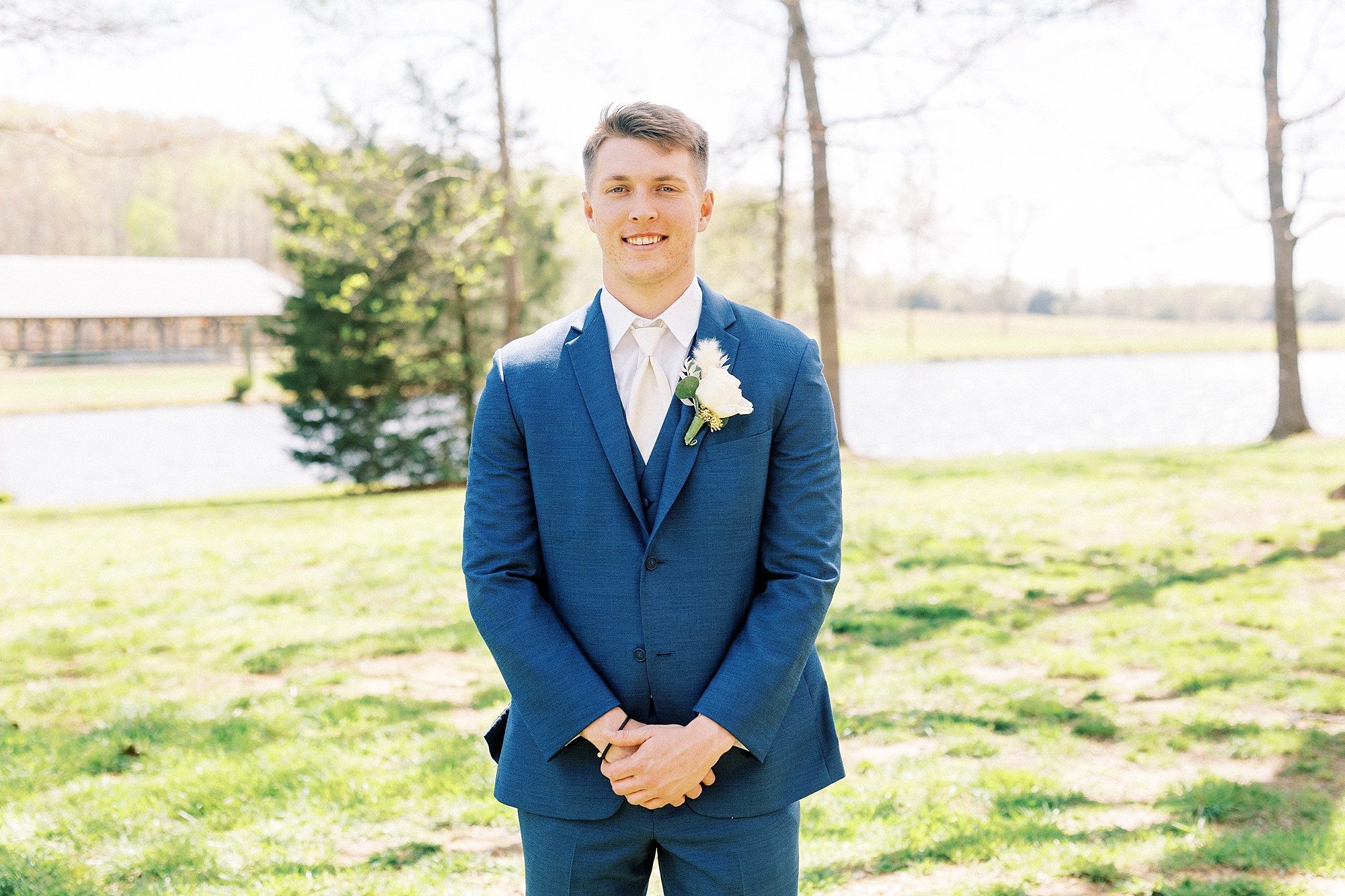 groom stands in navy suit with white boutonnière 