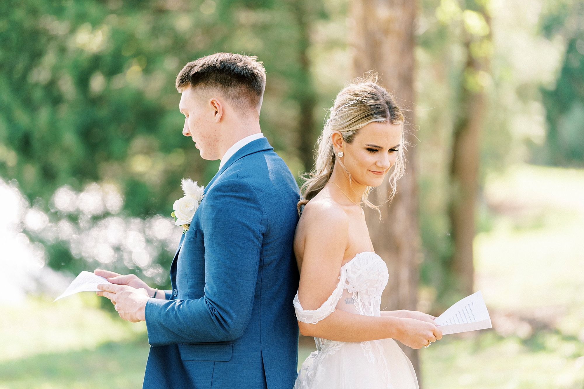bride and groom stand back to back reading vows to each other 