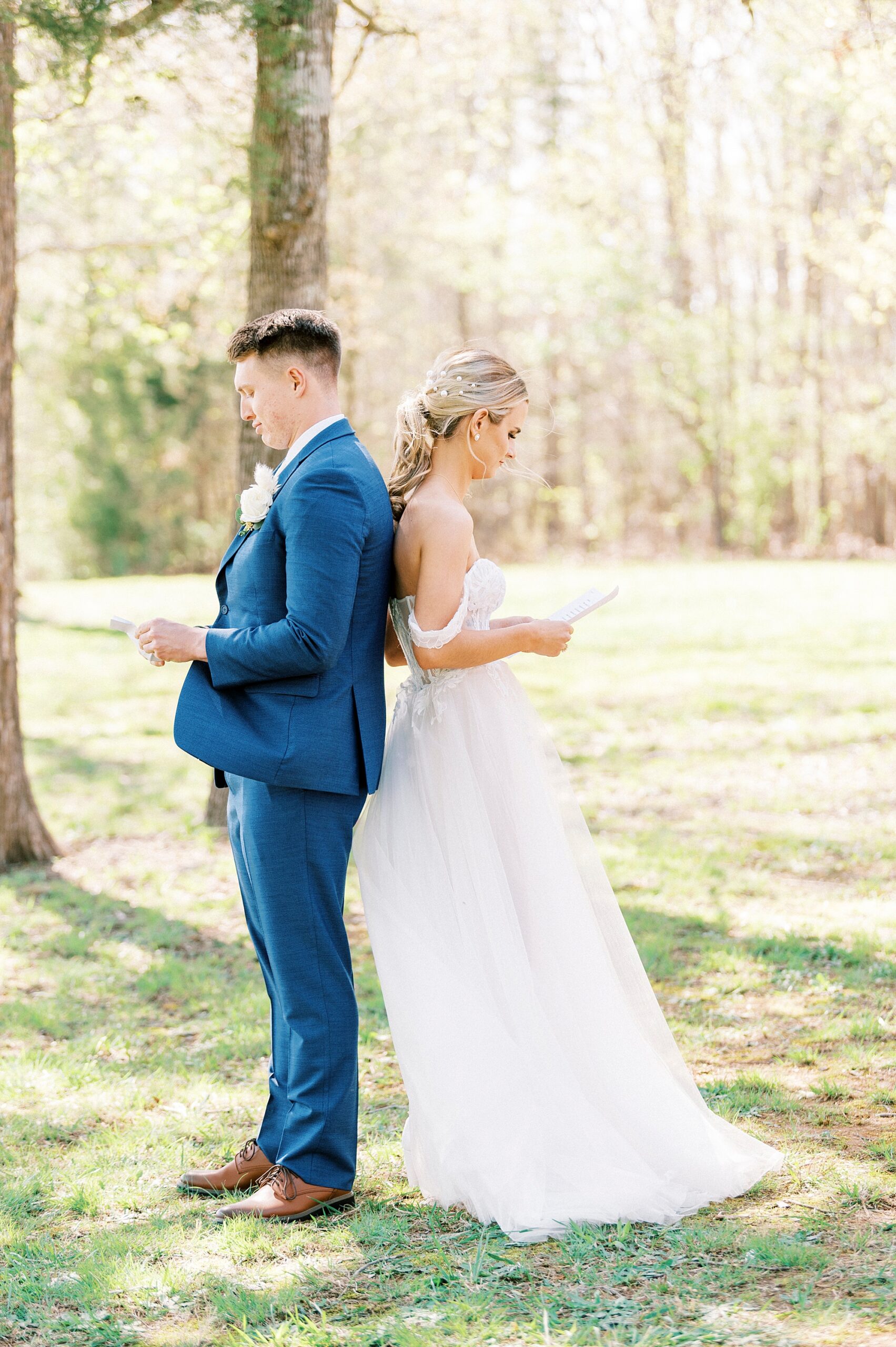 bride and groom stand back to back reading letters