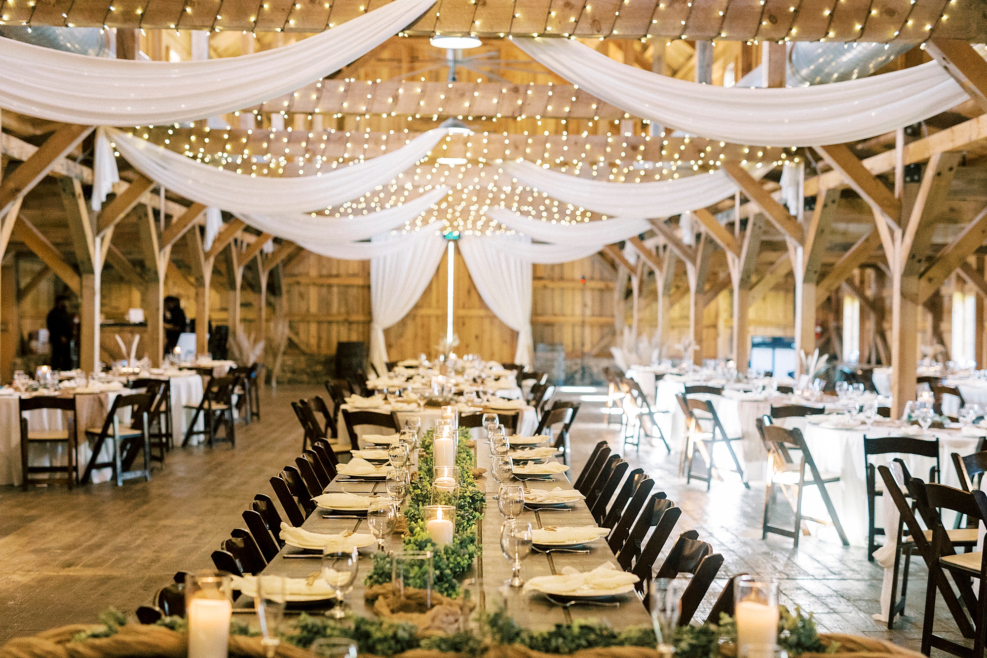 wedding reception at The Farmstead with burlap table runner and greenery with white fabric hanging from ceiling 