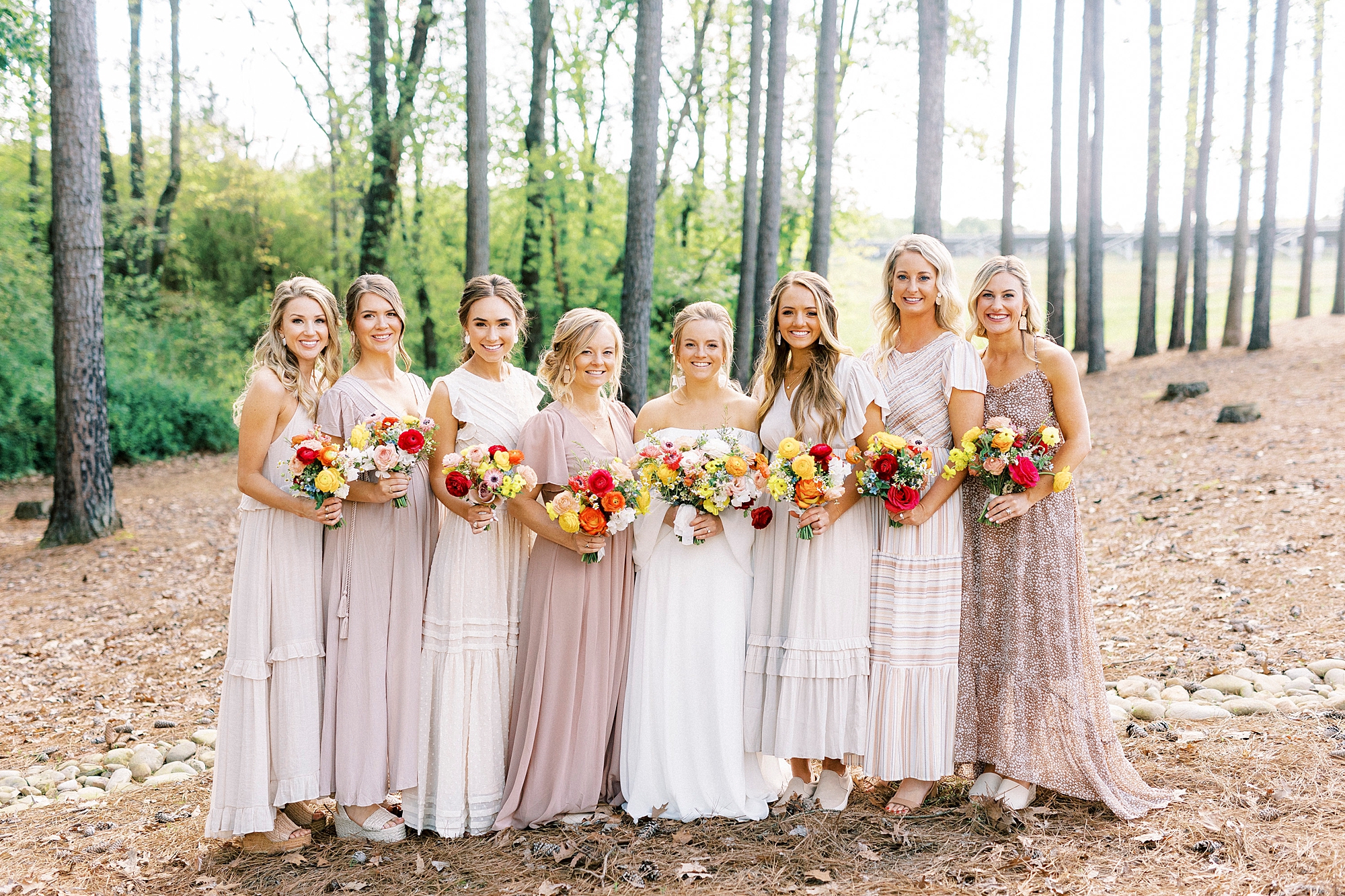 bride stands with bridesmaids in mismatched boho inspired bridesmaid gowns in pink