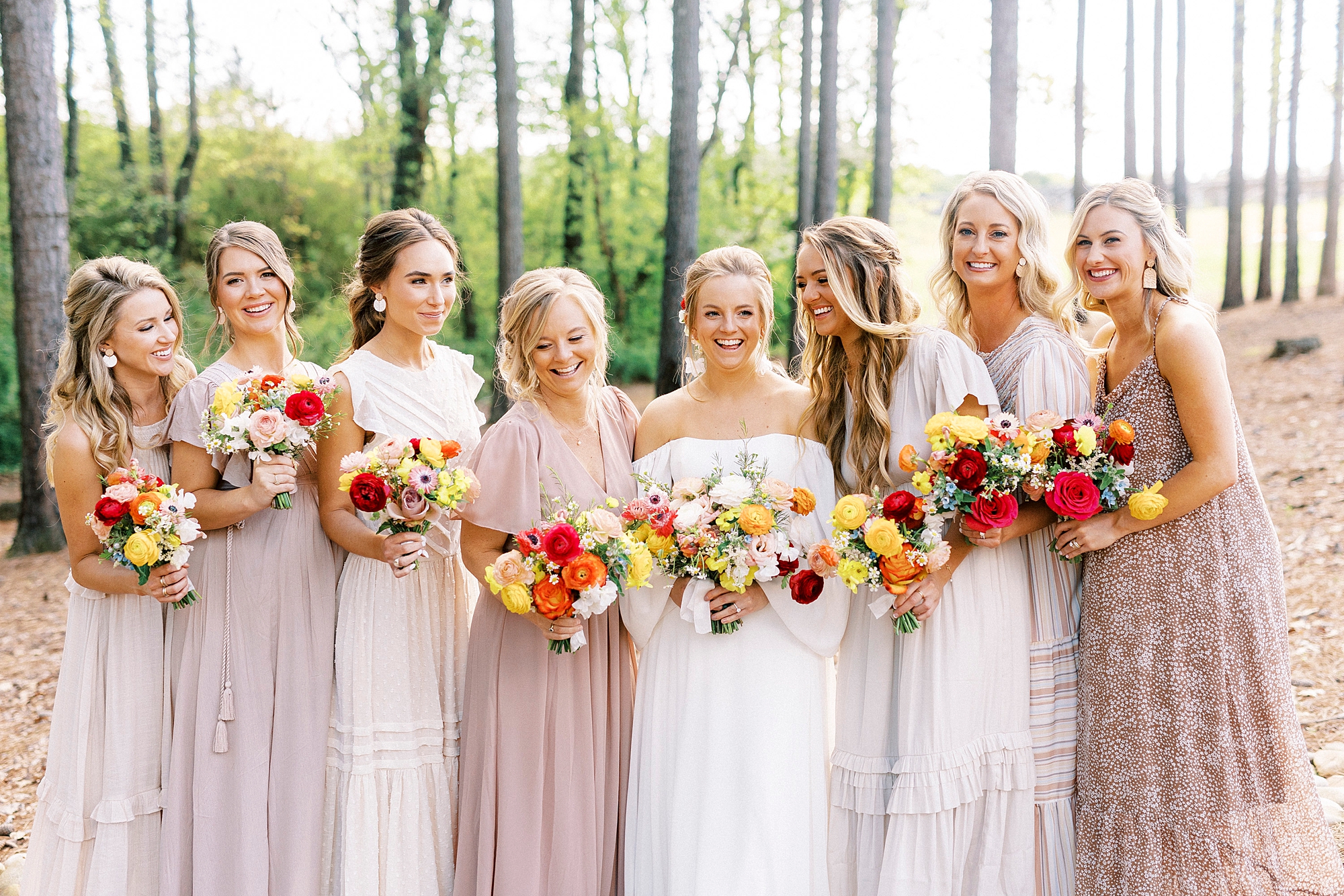 bride stands with bridesmaids in pink gowns with bright red and yellow flowers 