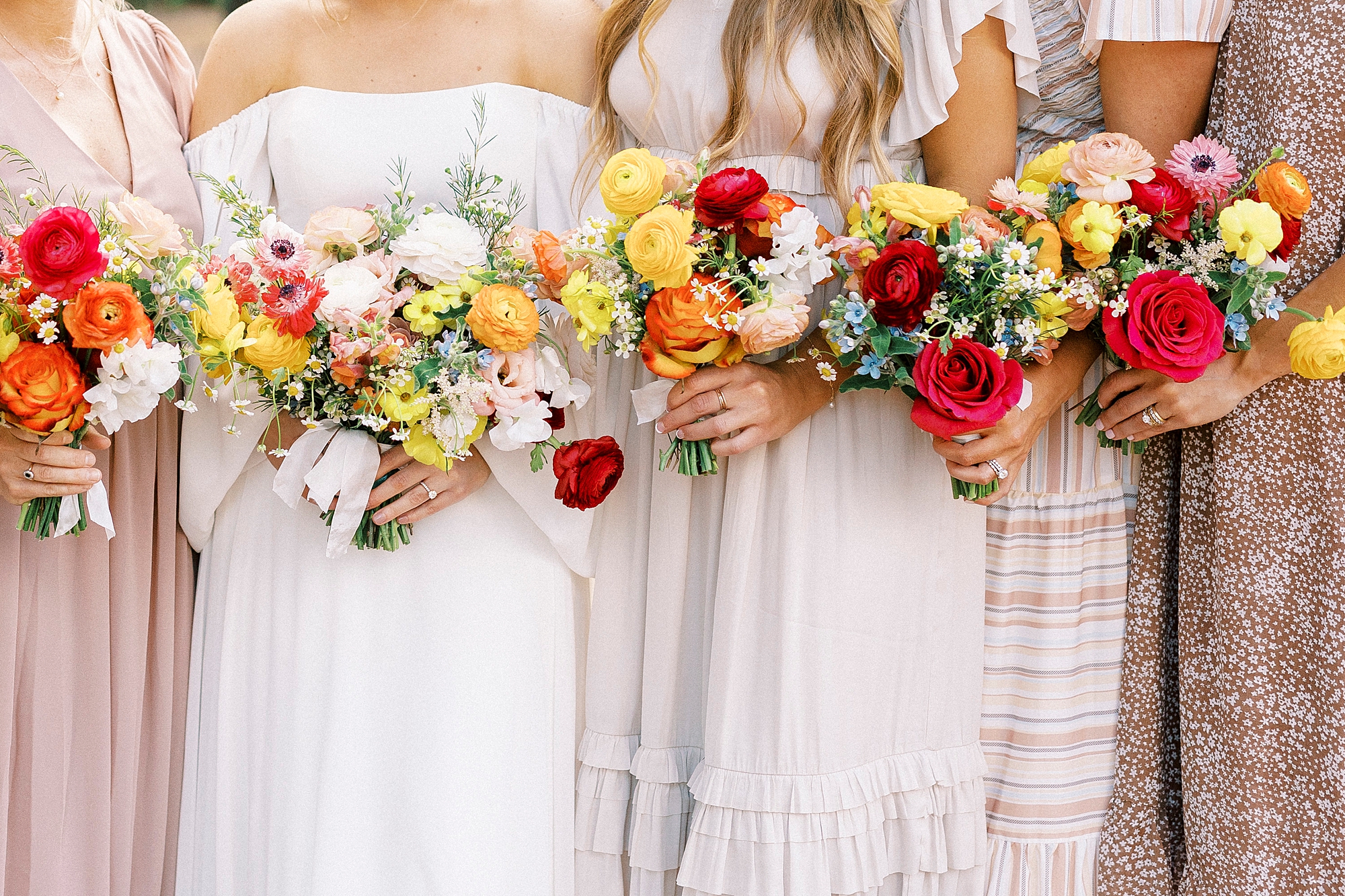 bridesmaids in pink gowns hold bouquets of red and yellow flowers 