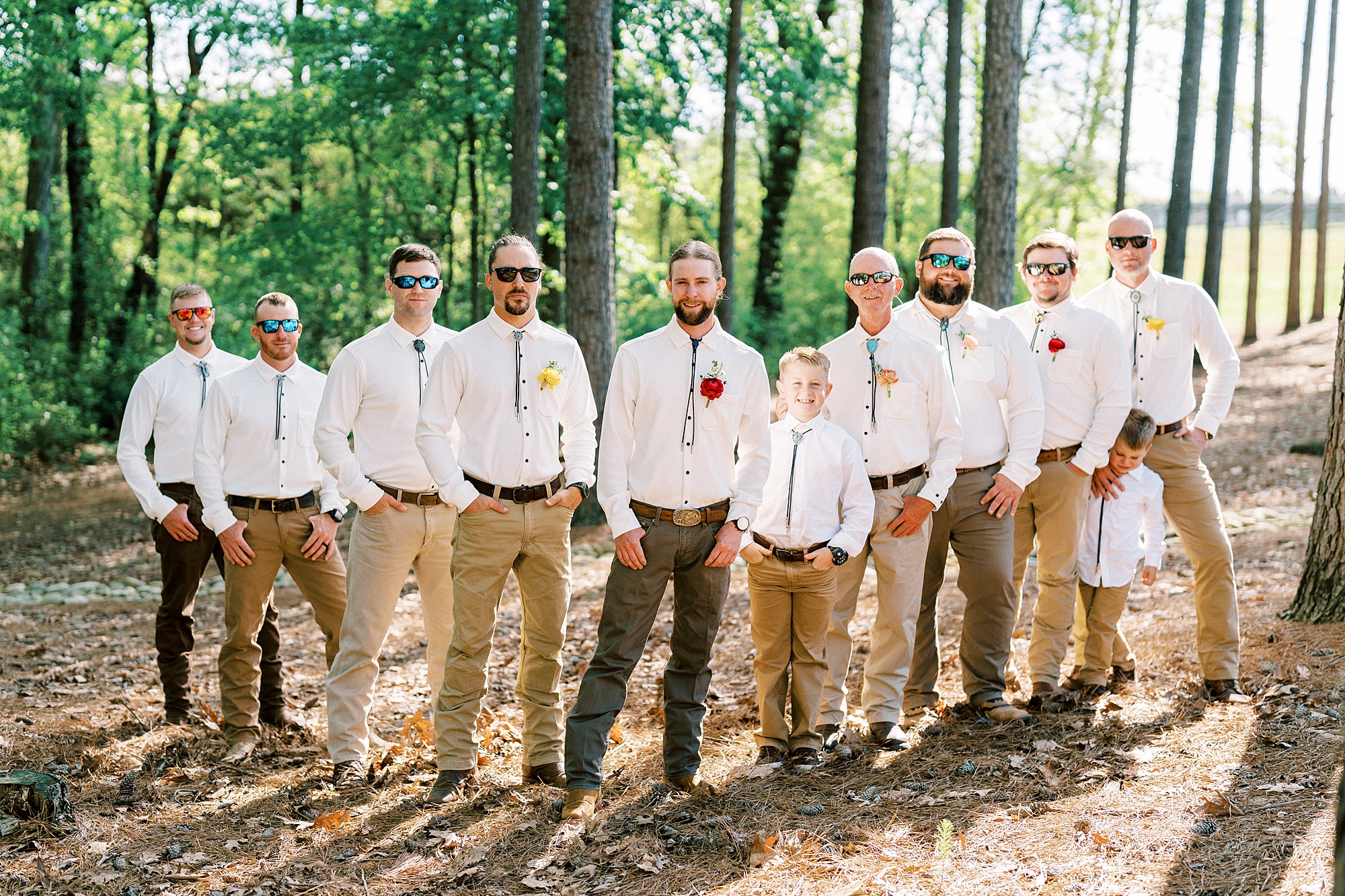 groom stands with groomsmen in white long sleeve shirts, tan pants, and bolo ties 