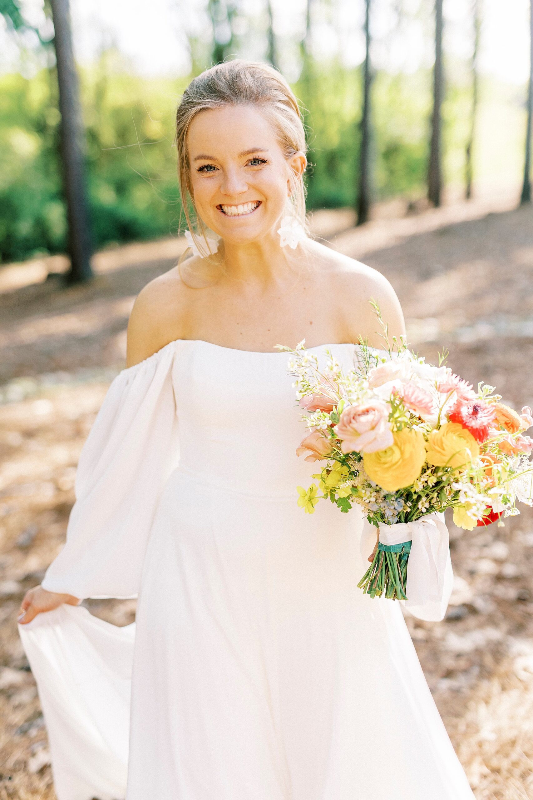 bride holds bouquet of yellow and red flowers in front of off-the-shoulder gown