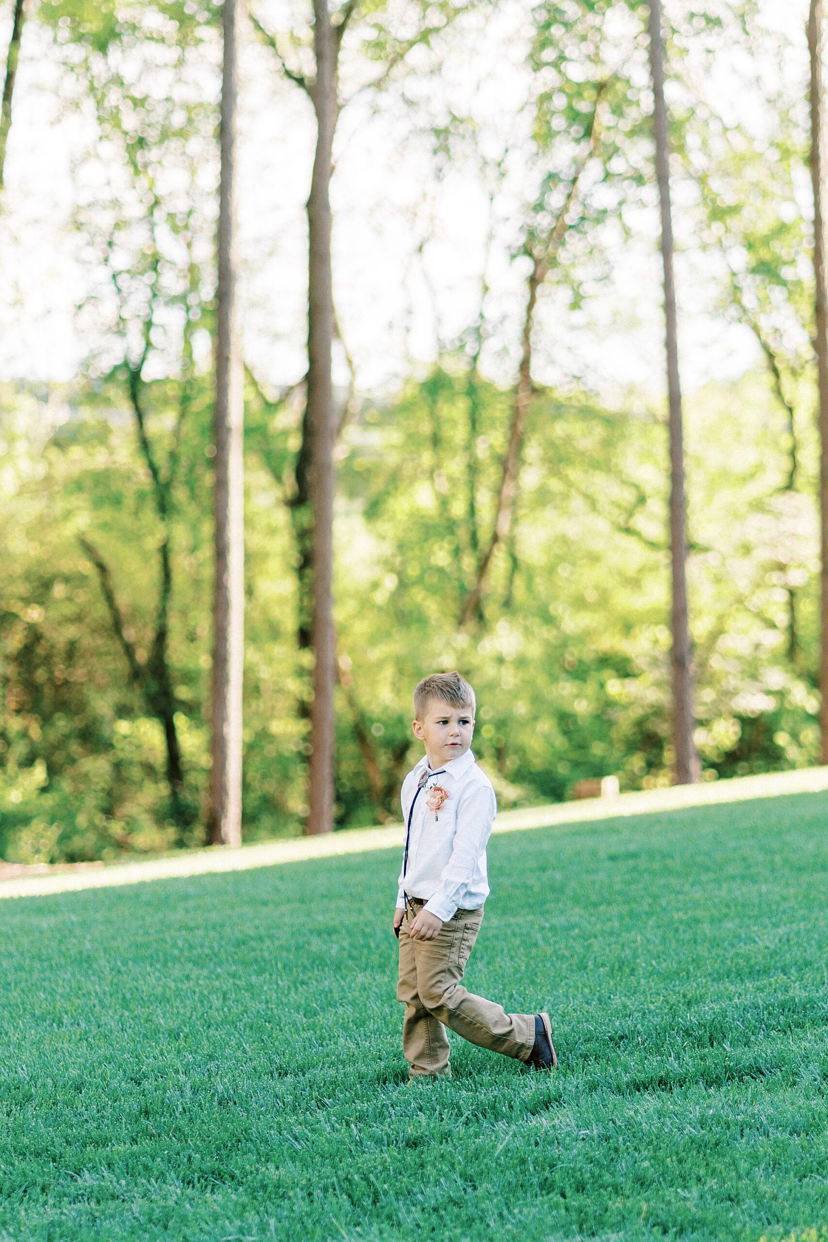 ring bearer walks down aisle with hands in pockets for boho wedding ceremony on lawn of Richfield NC home