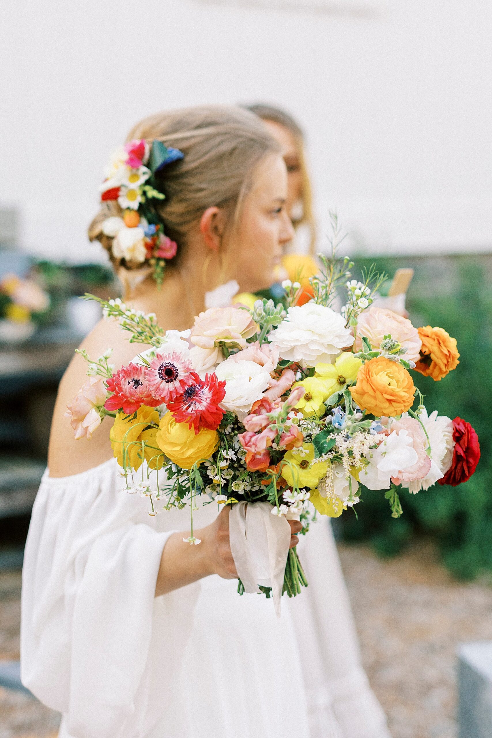 bride holds bouquet of bright pink, yellow, and orange flowers 